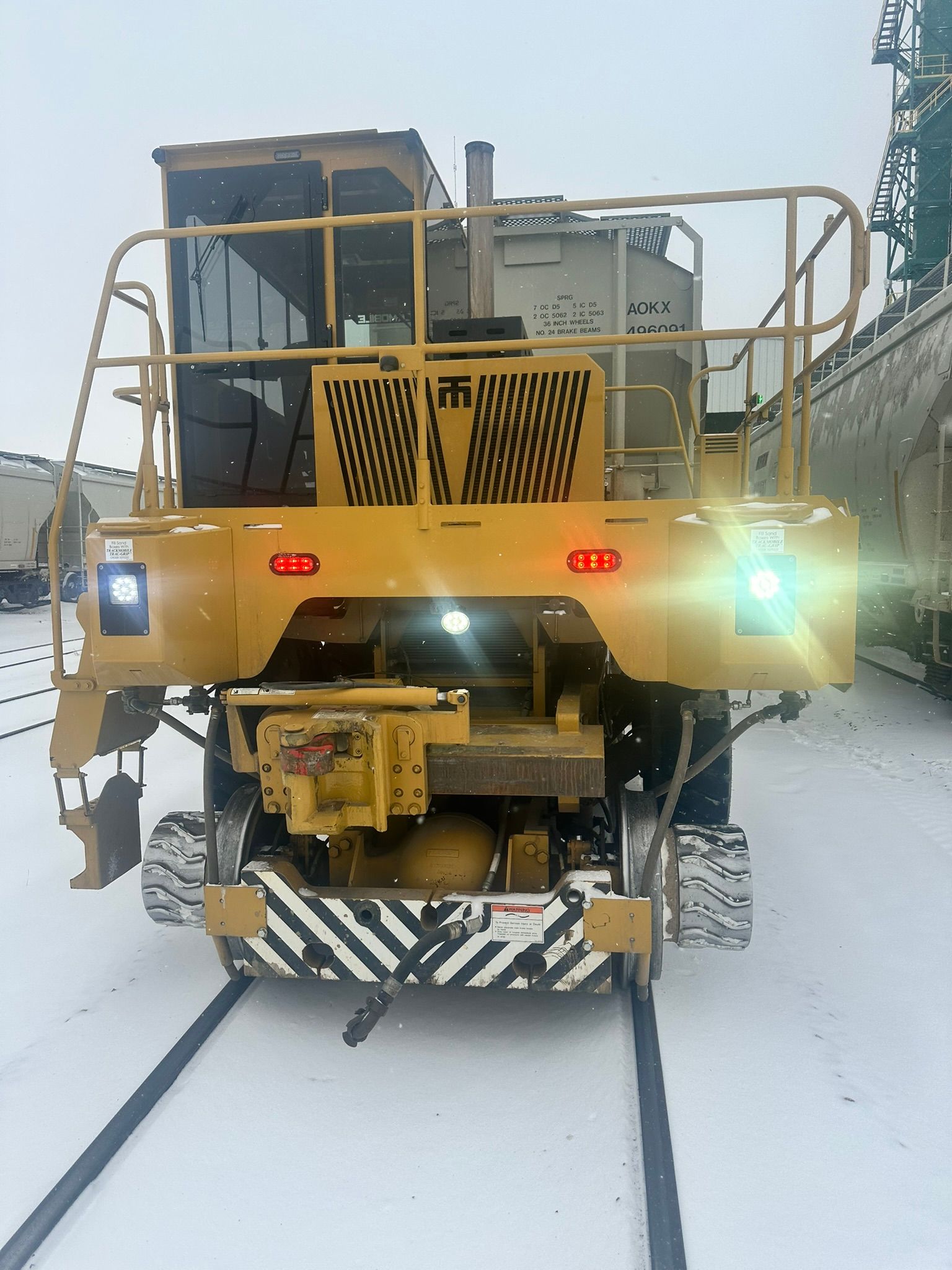 Yellow railway maintenance vehicle on tracks in snowy conditions.