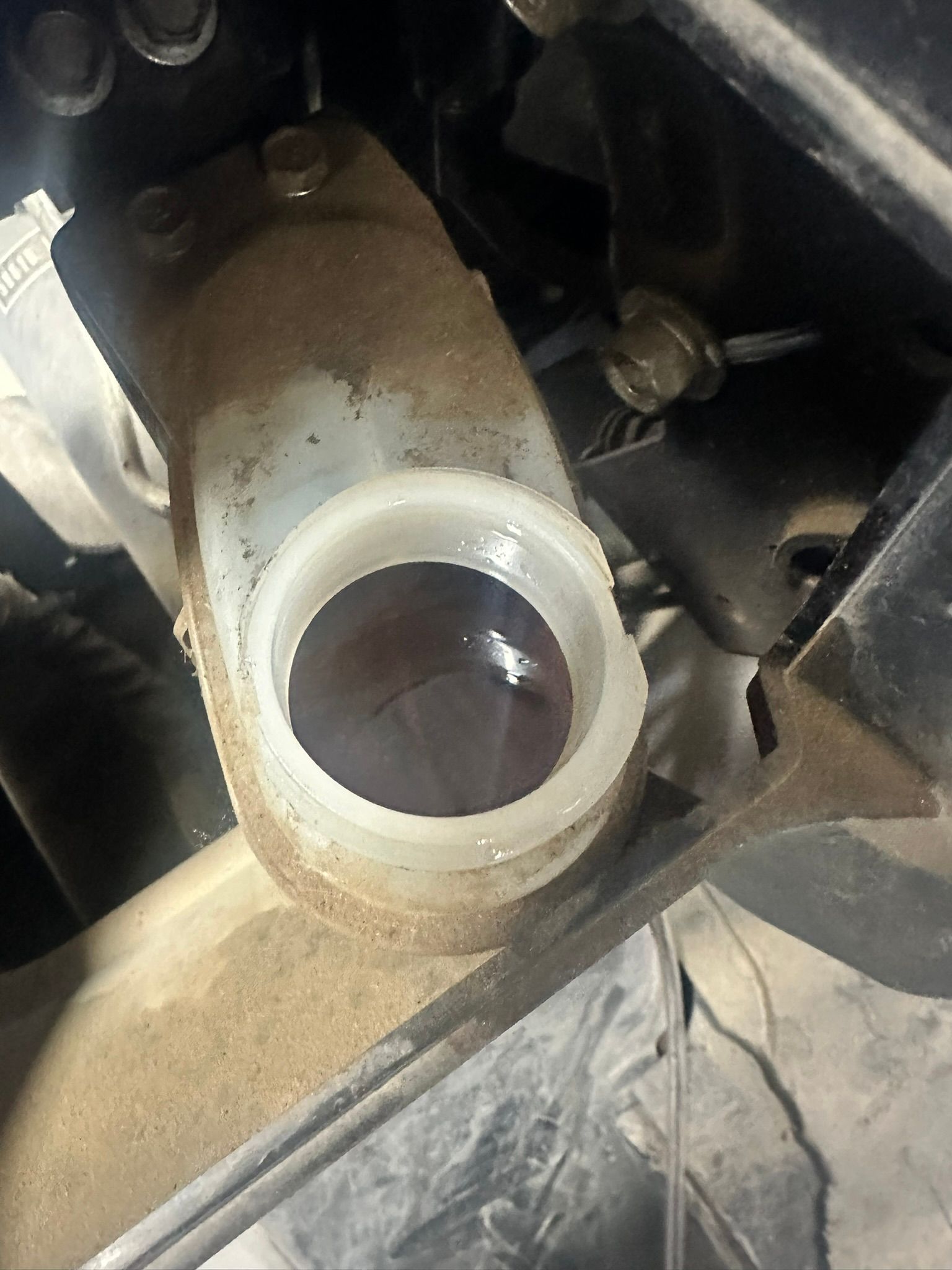 Brake fluid reservoir. Translucent plastic container with dark brake fluid inside, mounted in a dusty engine bay.