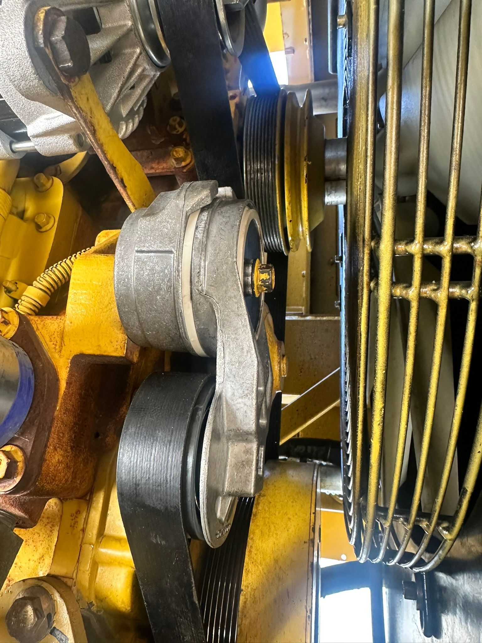 Engine components with black belt running over pulleys and tensioner, against a yellow background.