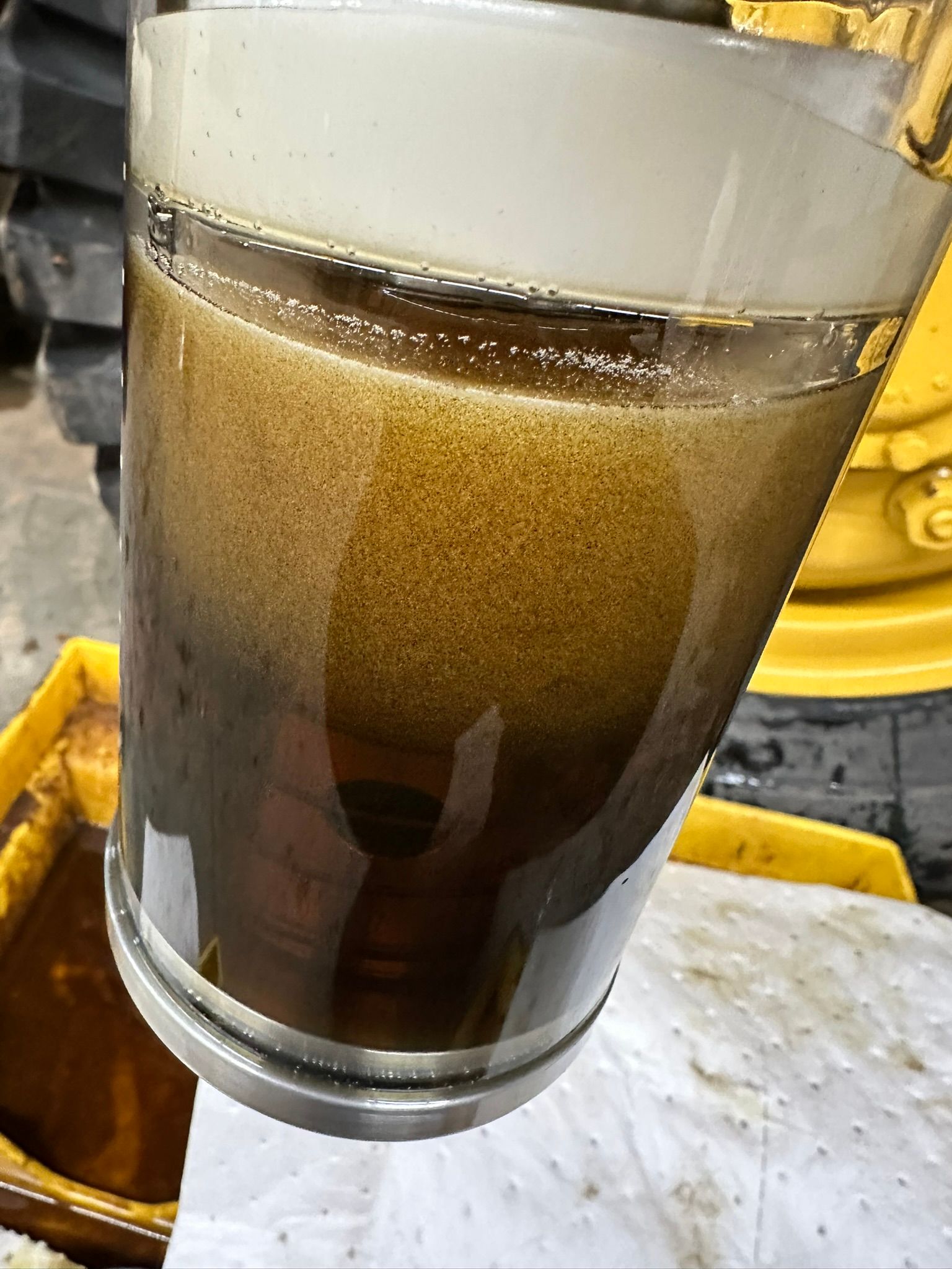 Glass container holding murky, dark brown fluid, possibly used engine oil.