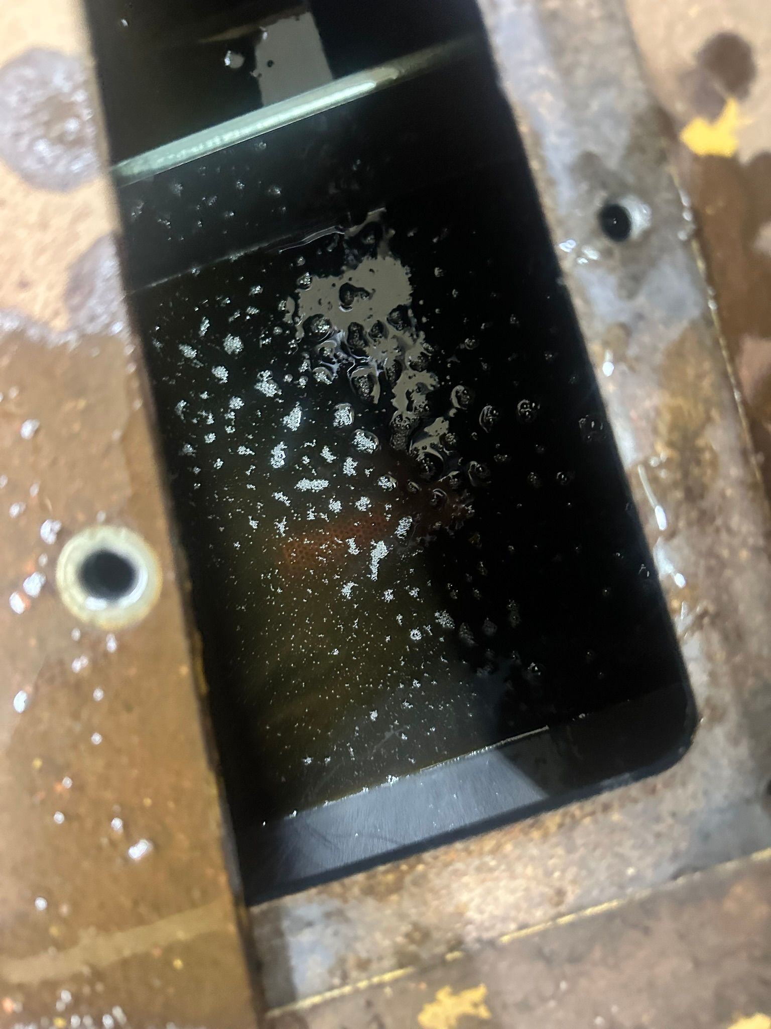 Black smartphone screen with water spots, resting on a metal surface.