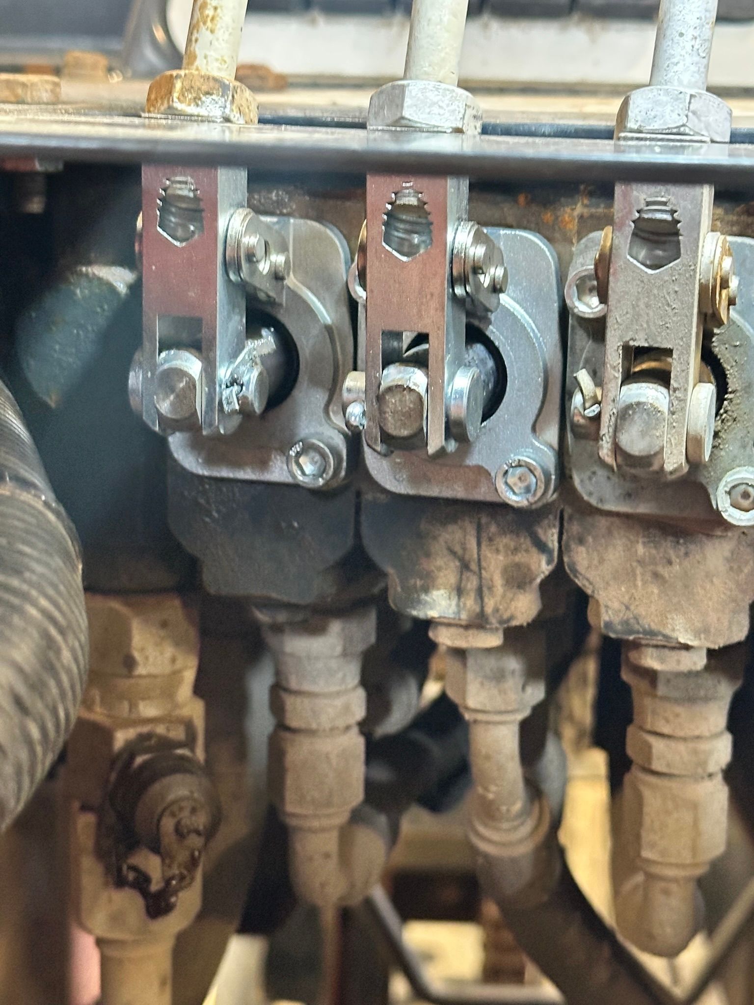 Close-up of three metallic electrical connectors, with copper colored sections, bolted to an apparatus with pipes.