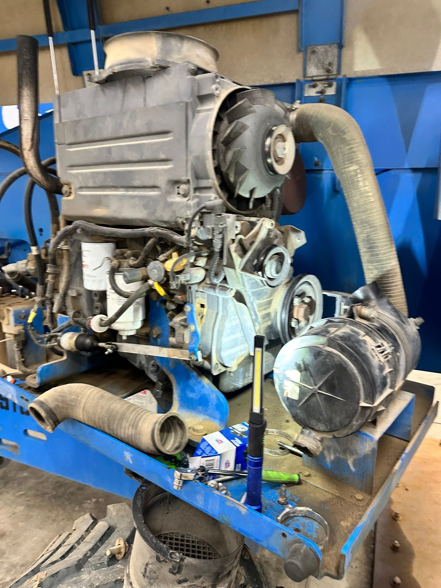 Engine components on a blue platform, with a large fan and several hoses, possibly under repair.