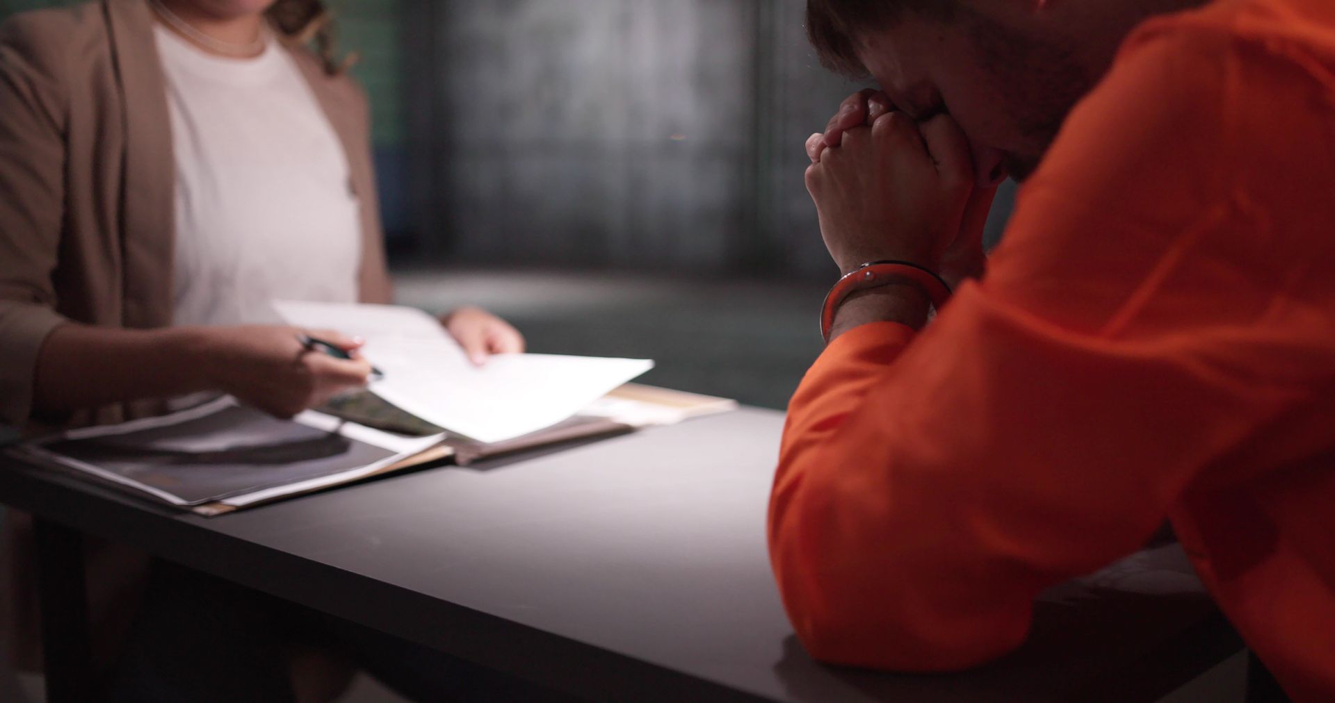 Two people at a table, one holding papers, in a dimly lit room.