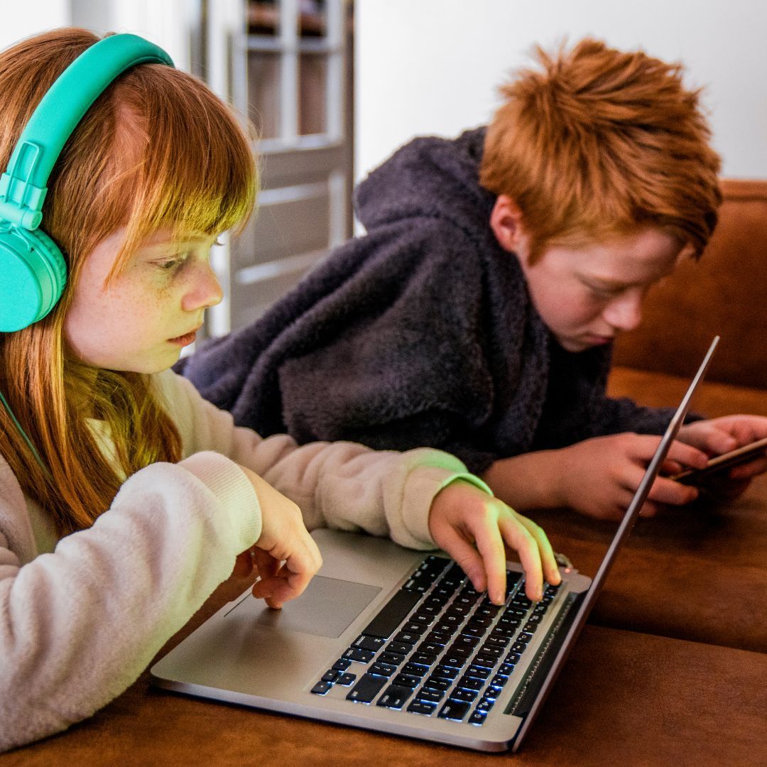 A Courageous Voice / Two siblings are sitting next to each other. The sister is on a laptop and the brother is on a smartphone. 