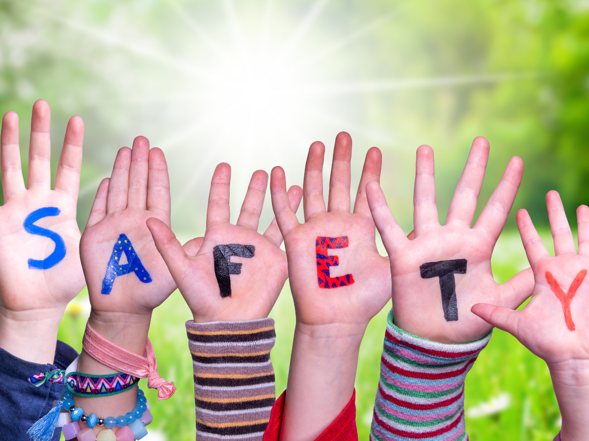 A group of children are holding up their hands to spell out the word safety.