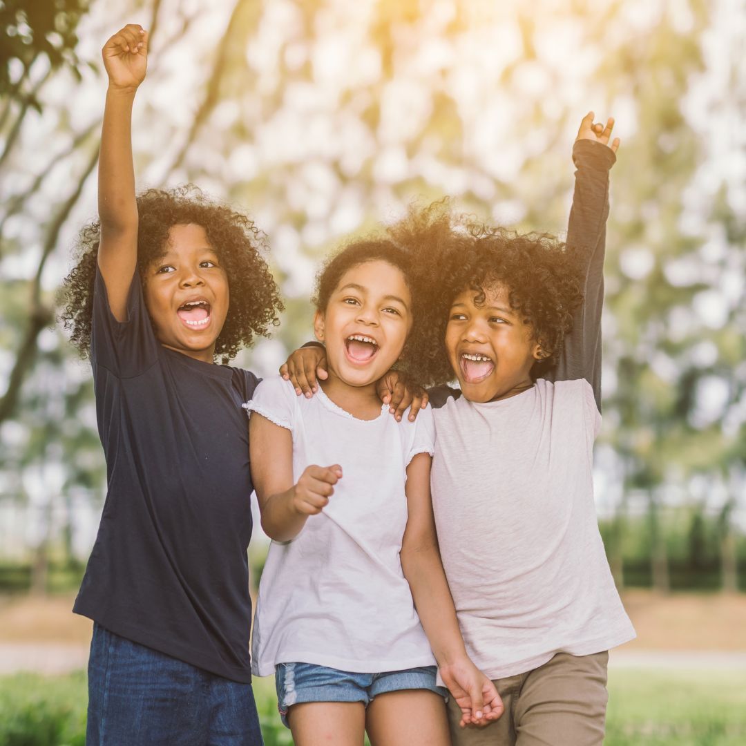 A Courageous Voice / A group of three children outside, smiling and holding each other close.