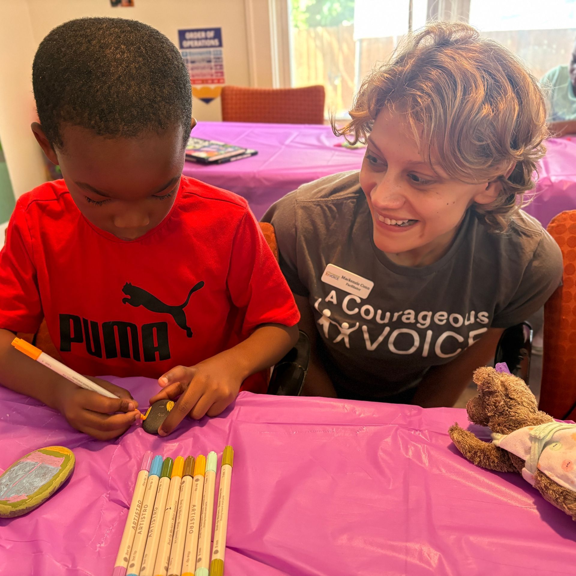 Two people at a purple table doing a craft activity with colored pencils and small pieces on the table