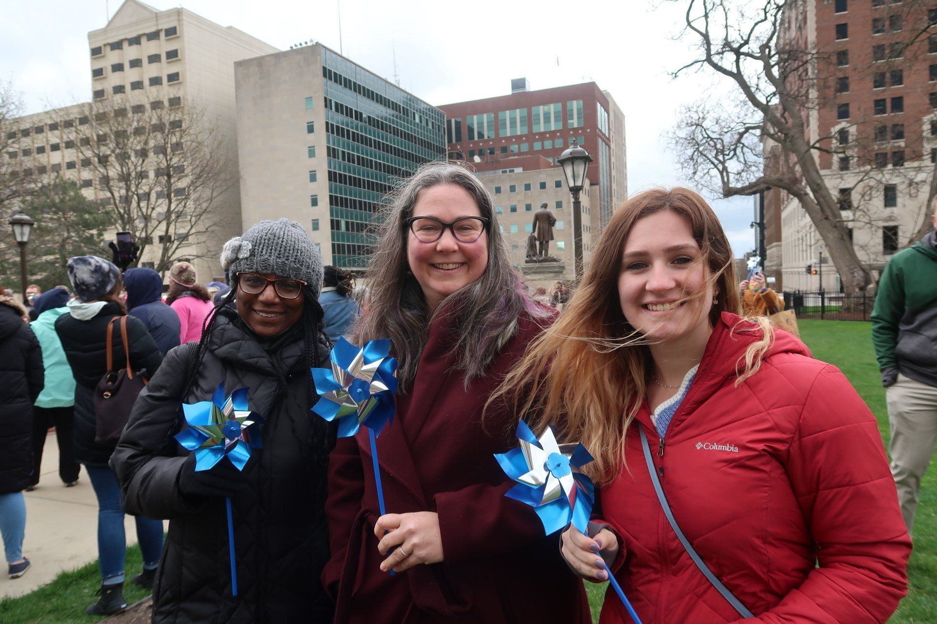 Three women are standing next to each other in a park holding windmills.