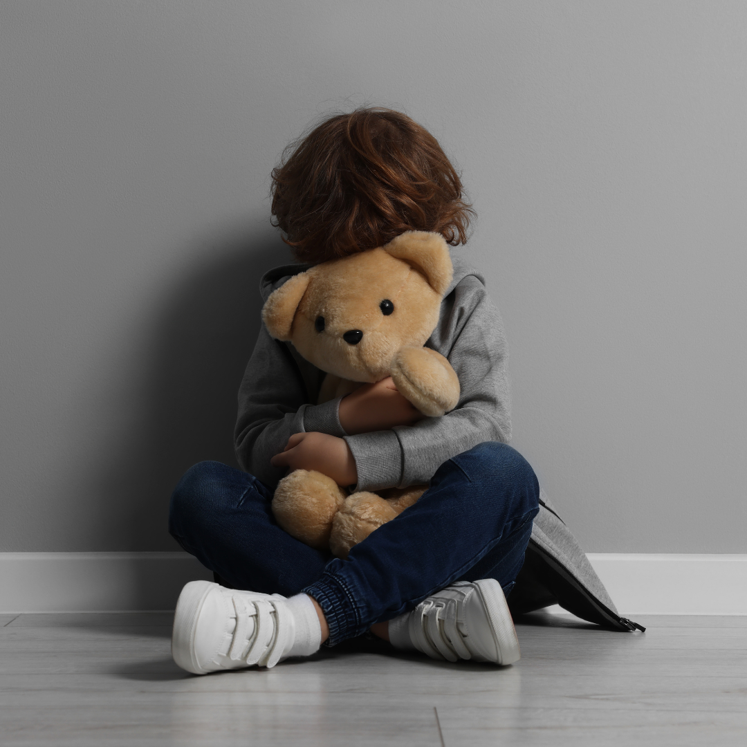 A Courageous Voice / A photograph of a young boy holding a large stuffed bear in front of his face and clinging to it. 