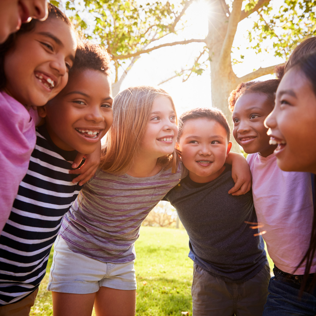 A Courageous Voice / A group of at least eight children of various races huddled together and smiling in a sunny, grassy area. 