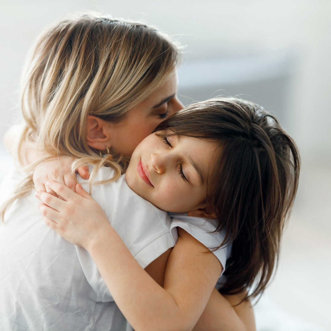 A Courageous Voice / A young girl with dark brown hair hugging her mother and closing her eyes, looking relaxed. 