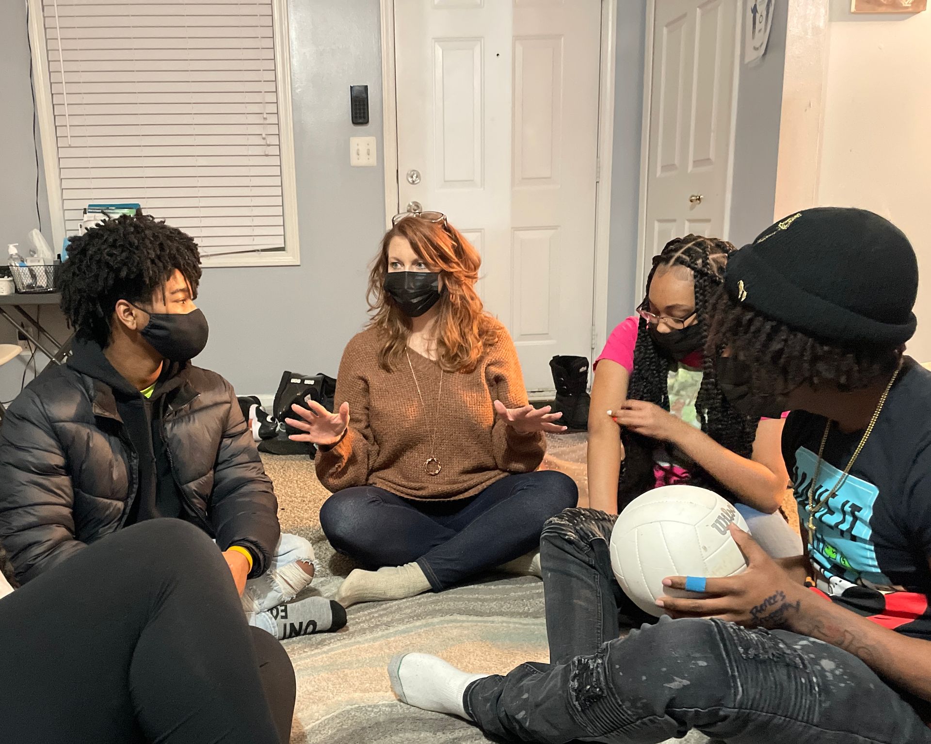 A group of people wearing masks are sitting on the floor in a living room.