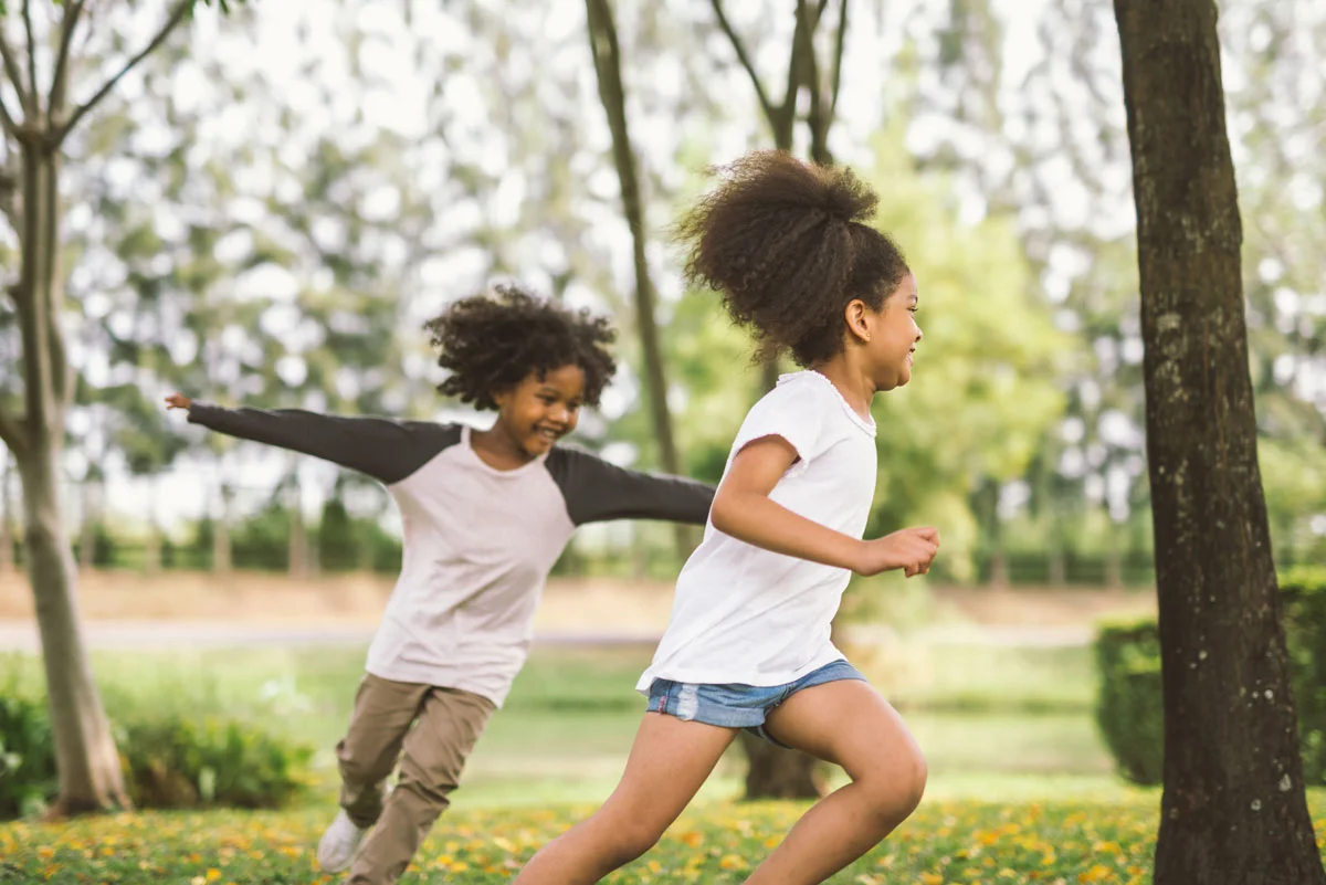 A boy and a girl are running in a park.