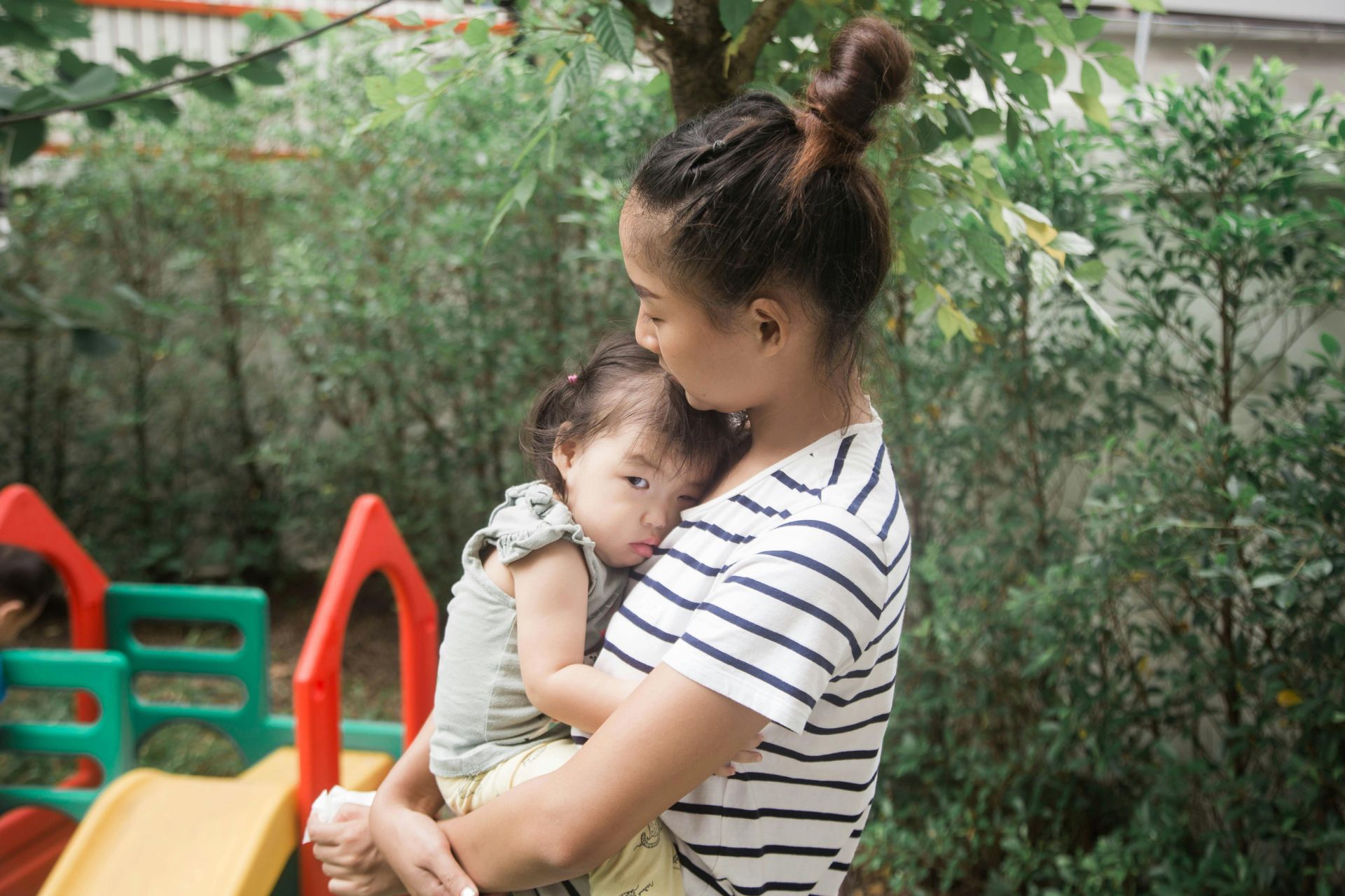 Woman holding a sleeping child outdoors in a garden area