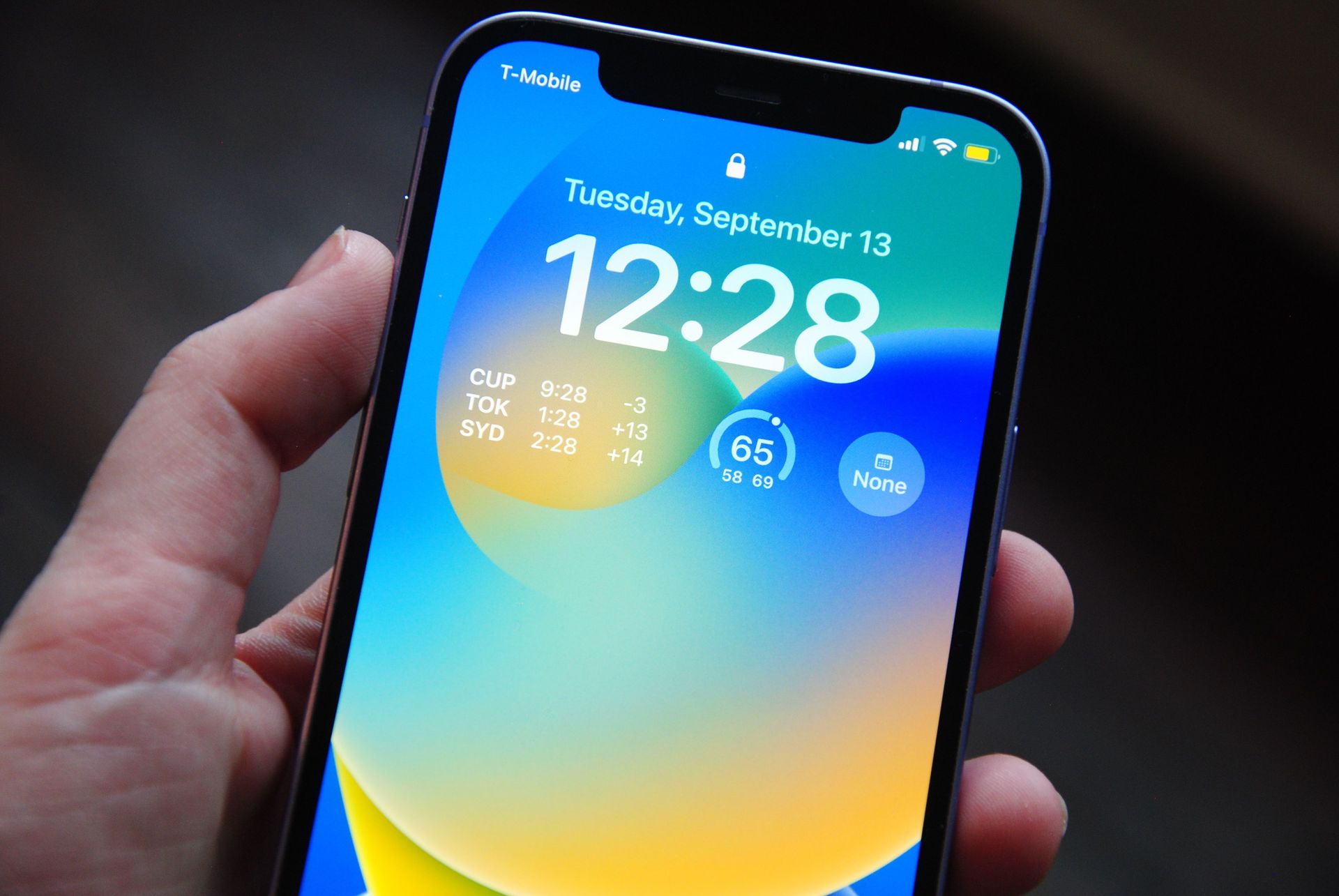 Hand holding a smartphone with a colorful lock screen showing 12:28 and Tuesday, September 13.
