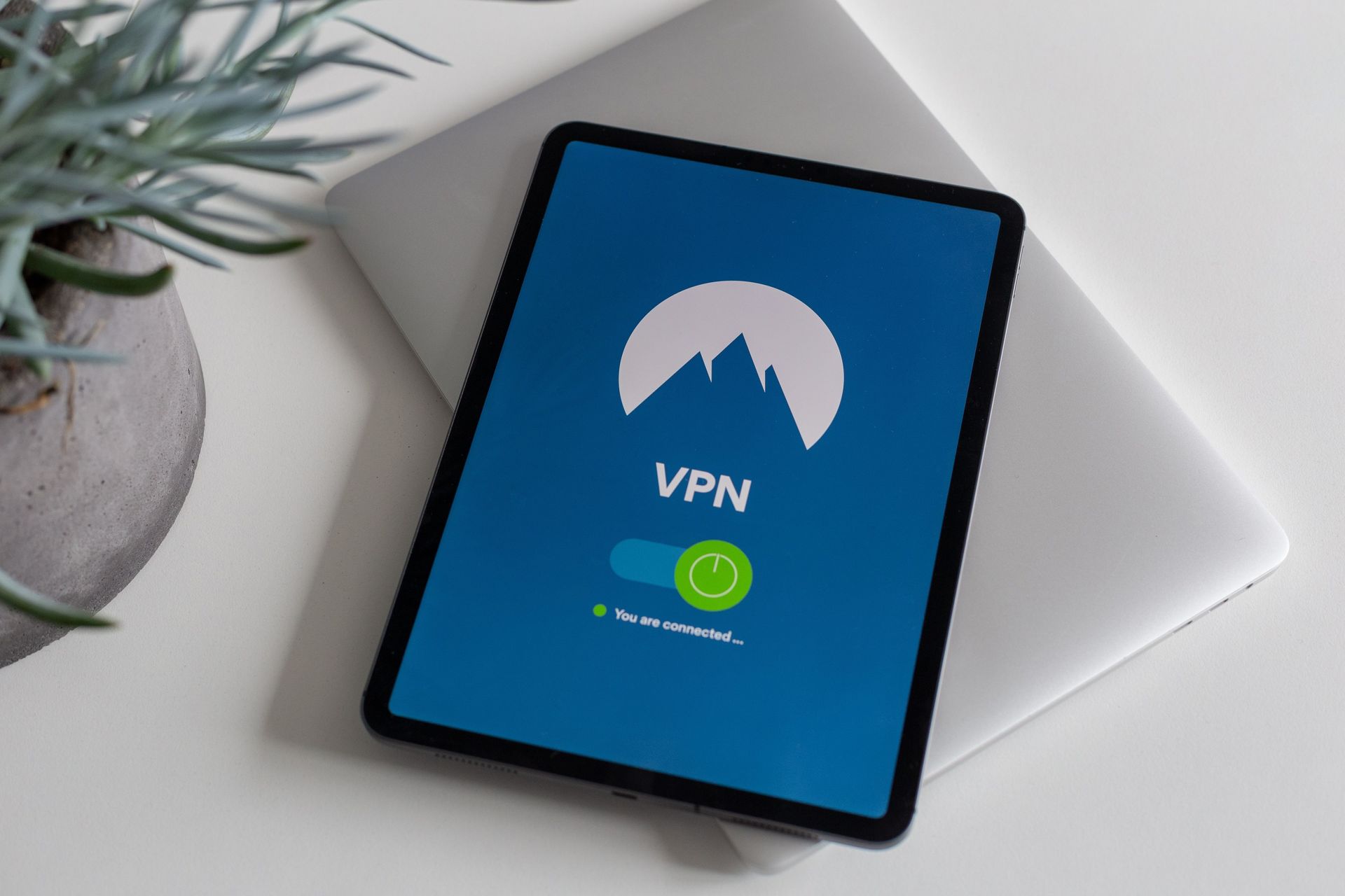Tablet displaying a VPN app on a white desk beside a plant and laptop