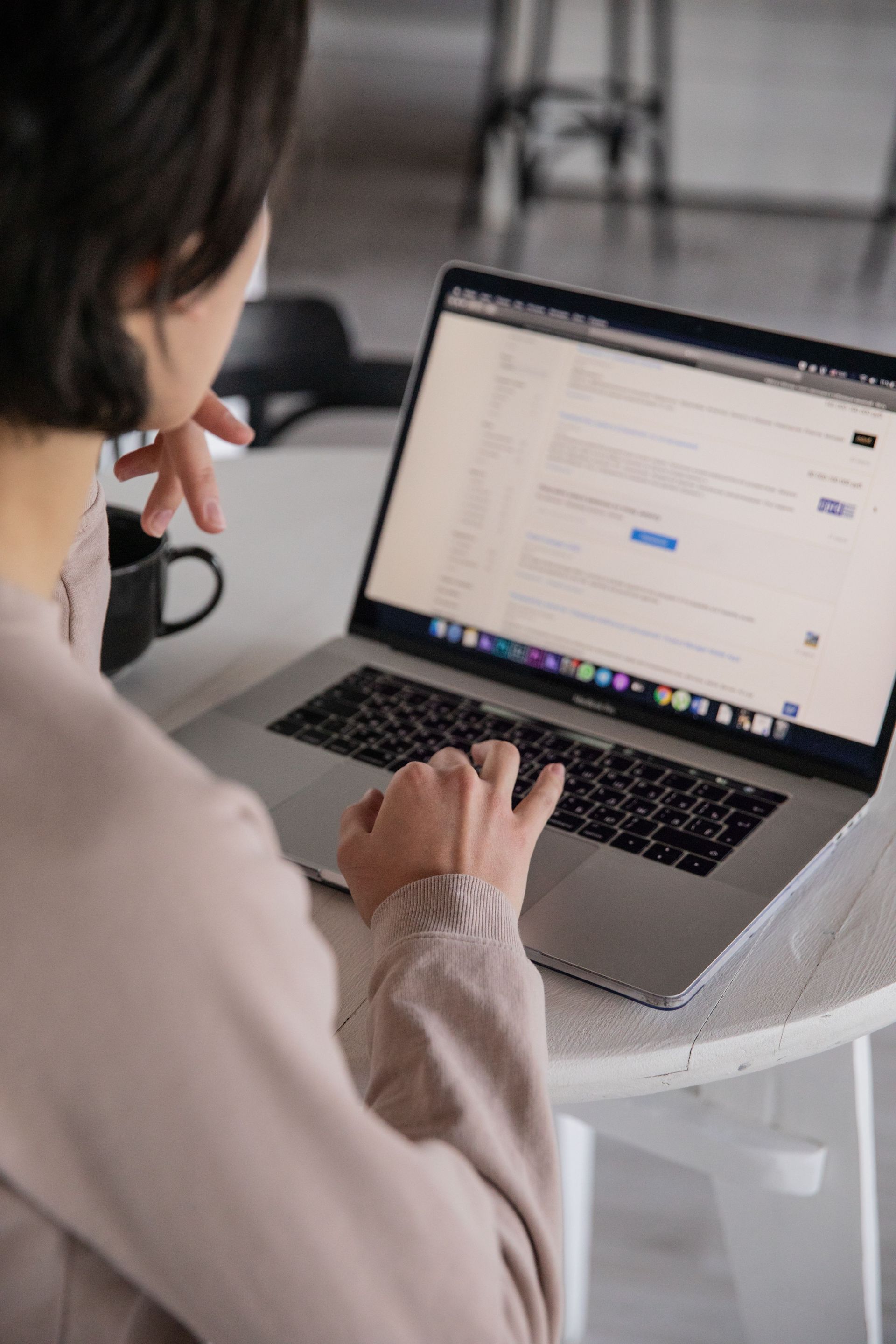 Person using a laptop at a white table, viewing a webpage while resting one hand on their face