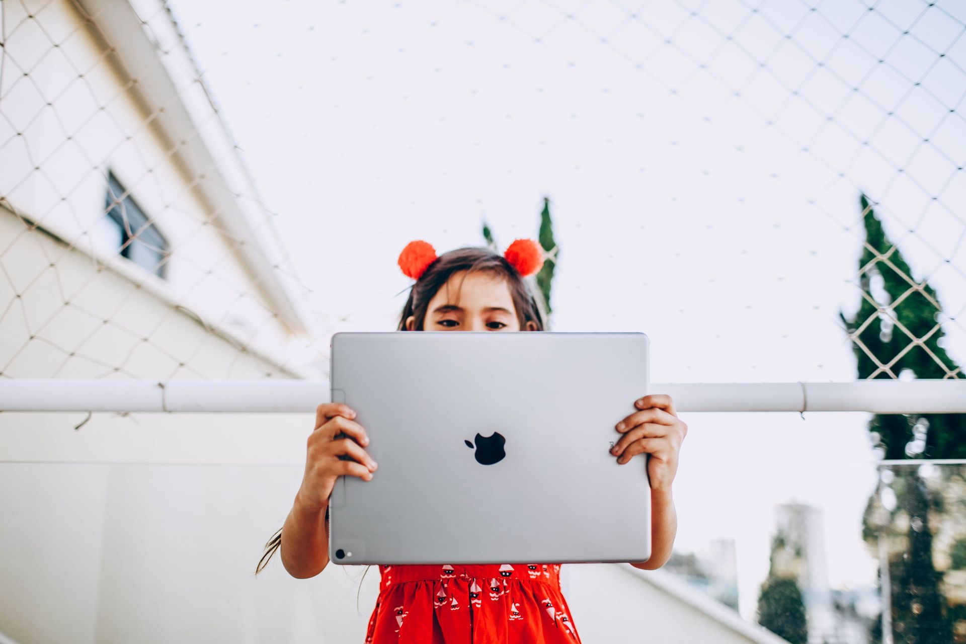 Child in a red dress holding a silver laptop outdoors.