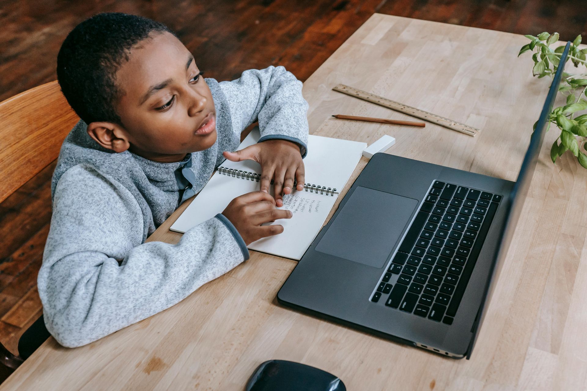 Boy looking at laptop and notebook on a wooden desk.
