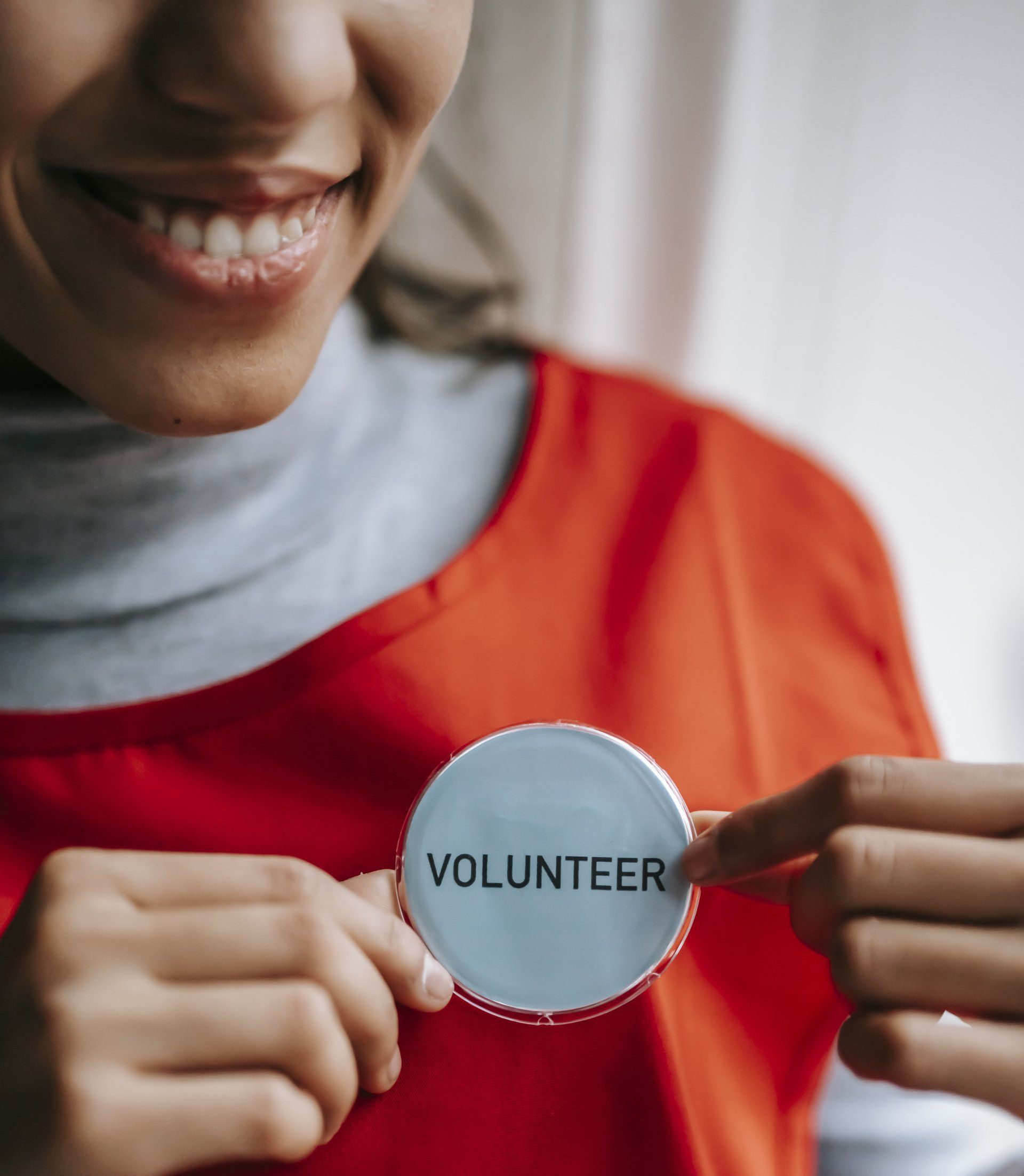 A woman in a red shirt is holding a volunteer badge