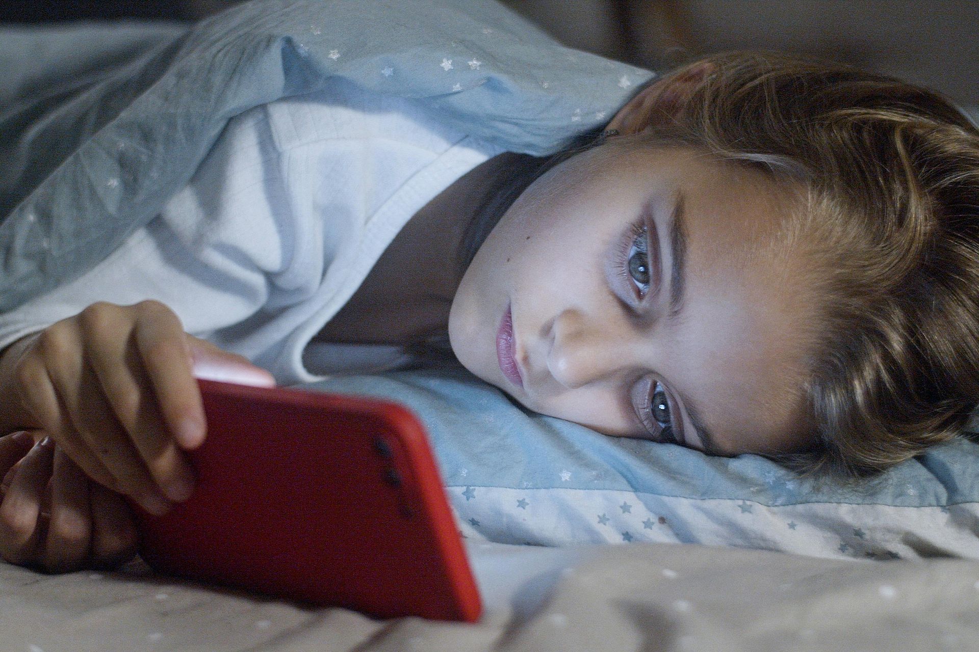 Child in bed, illuminated by a red phone screen.