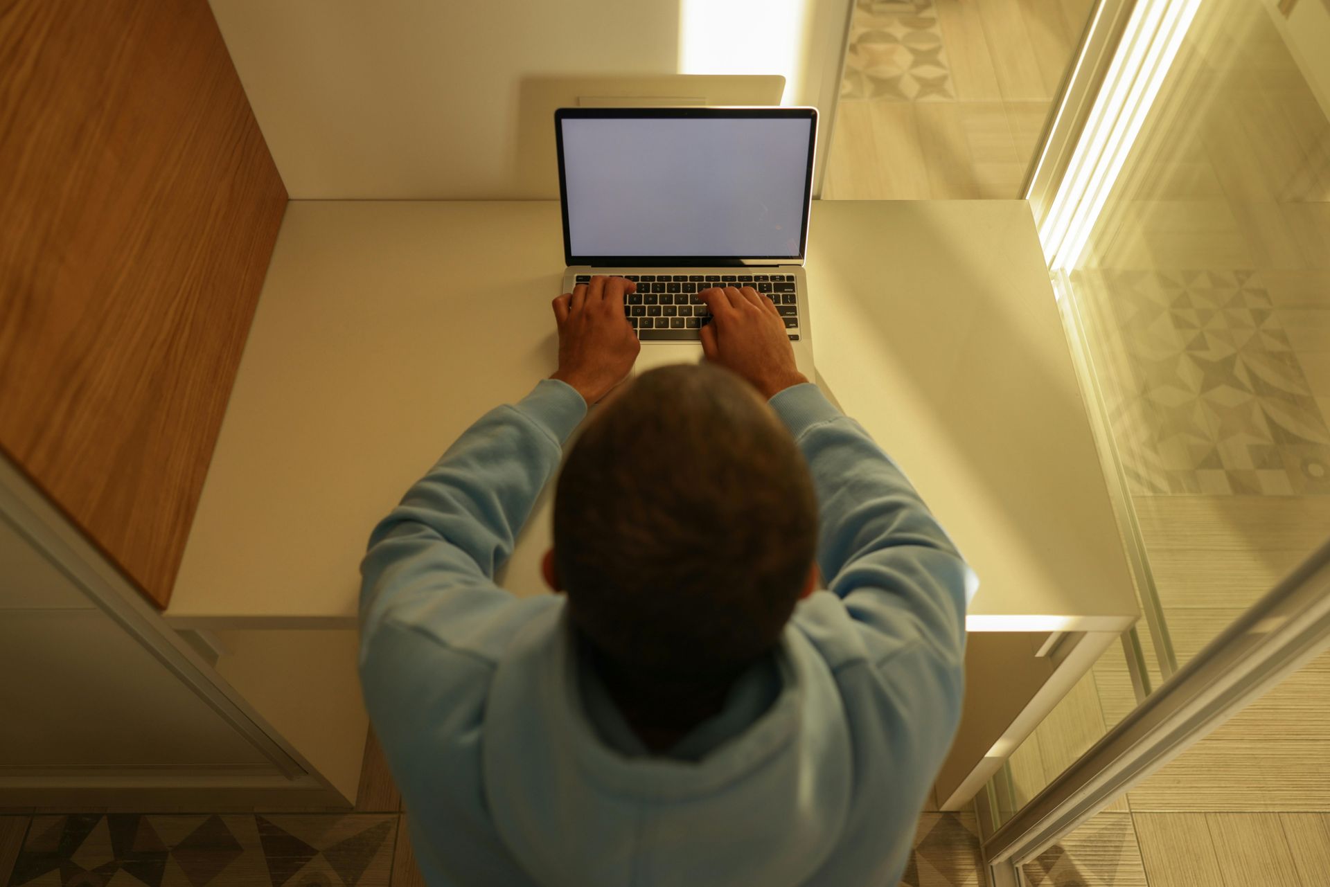 Person typing on a laptop at a desk in a bright room, viewed from above.