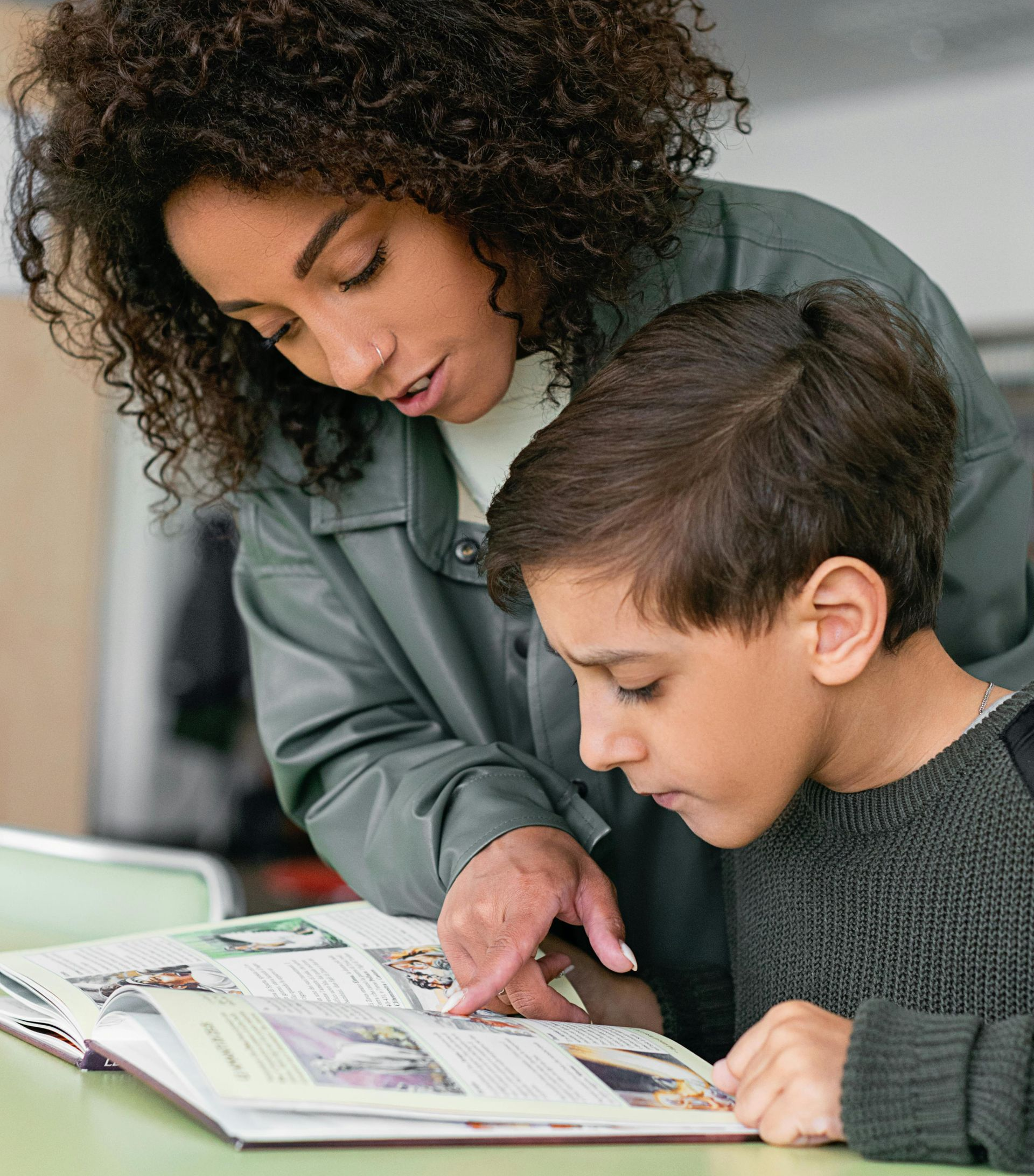 Woman points at book with boy; they're at a table, looking at pages.