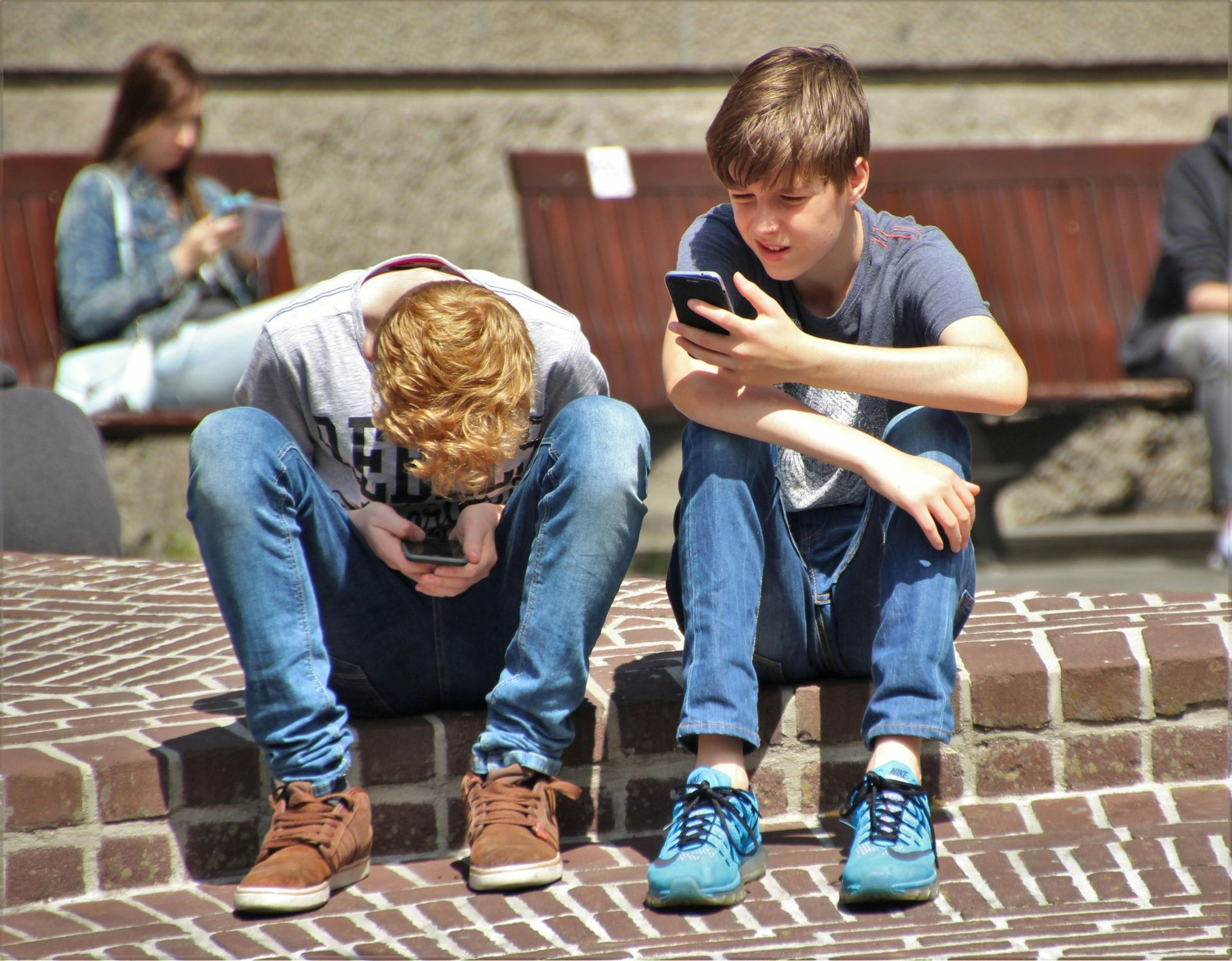 Two boys are sitting on a brick wall looking at their phones.