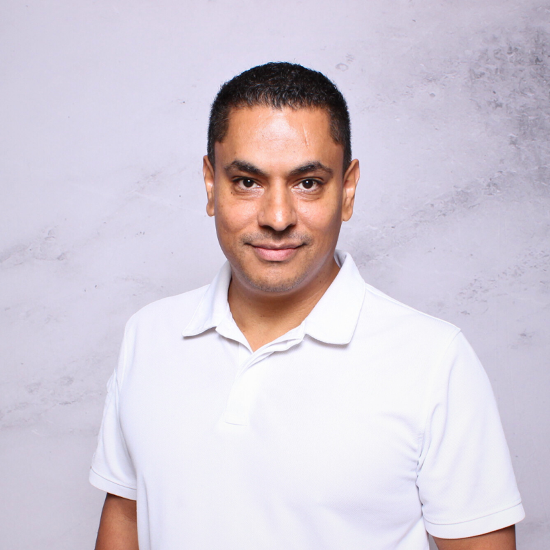 A man in a black shirt is standing in front of a tree.