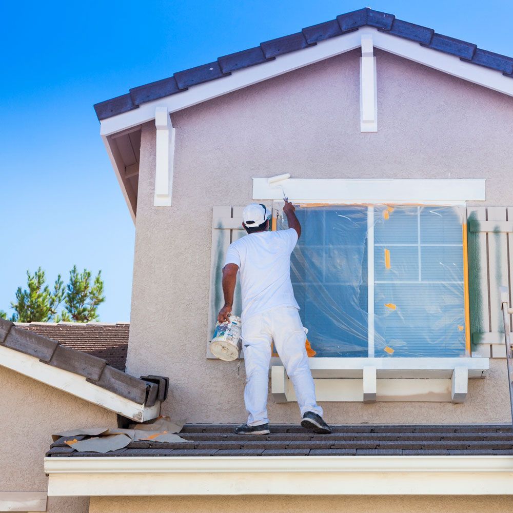 A man is painting a window on the side of a house