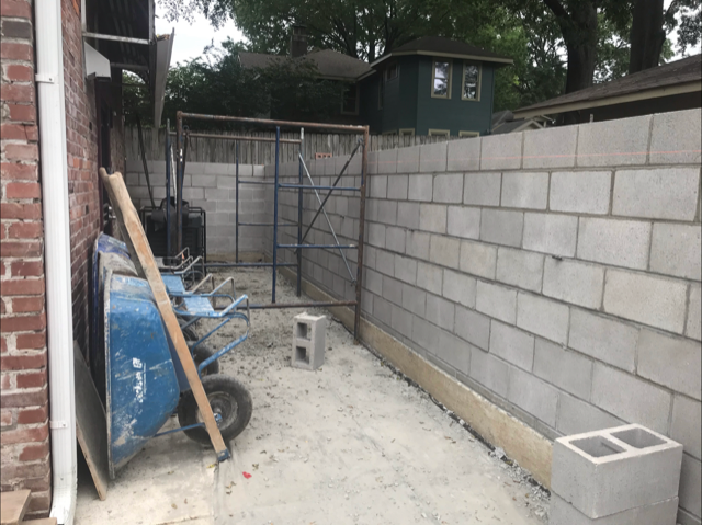 A wheelbarrow is sitting in front of a brick wall being built.