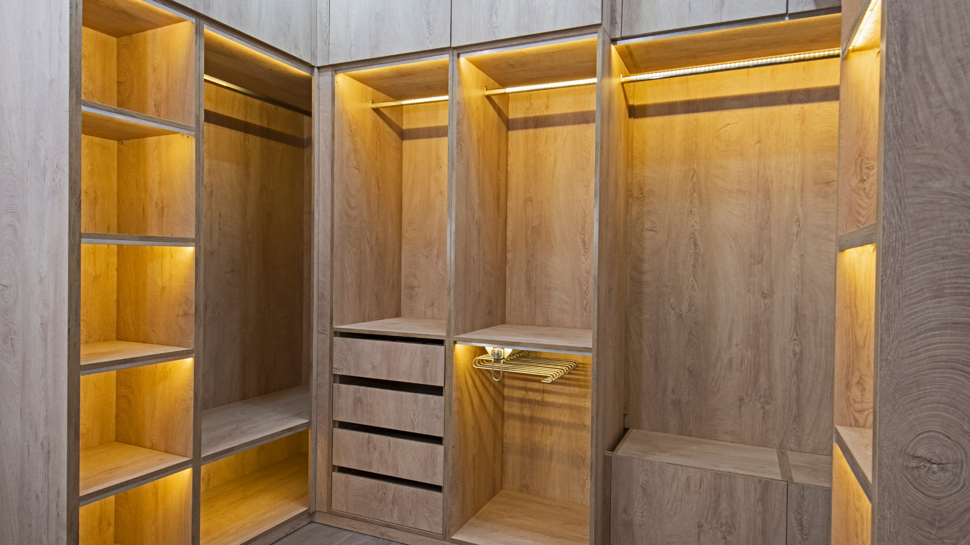 A walk in closet with wooden shelves and drawers and lights on the shelves.
