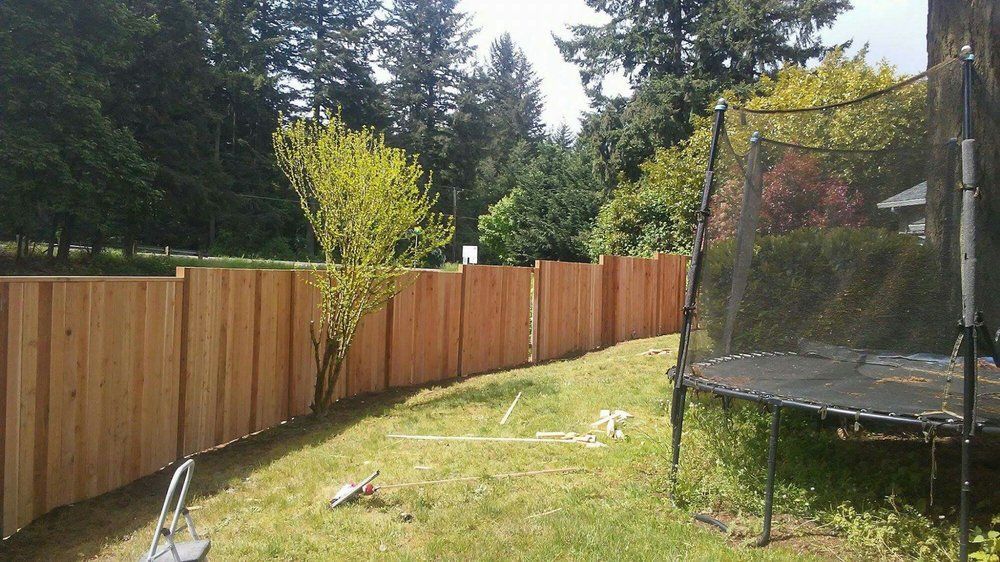 A wooden fence surrounds a backyard with a trampoline.