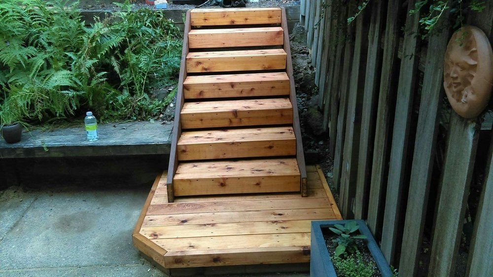 A wooden staircase is sitting on top of a wooden deck next to a wooden fence.