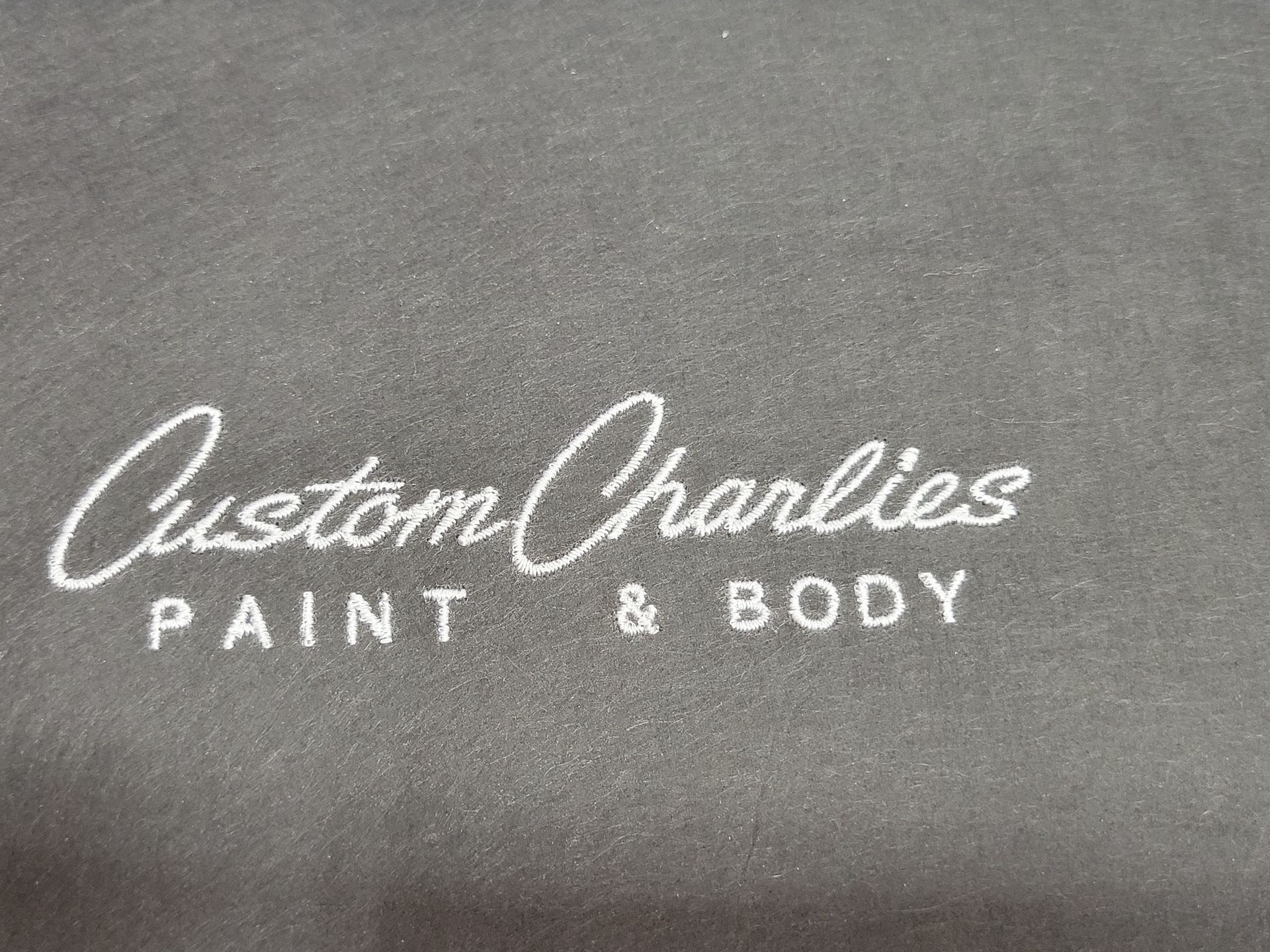 The logo for custom charles paint and body is embroidered on a black shirt.