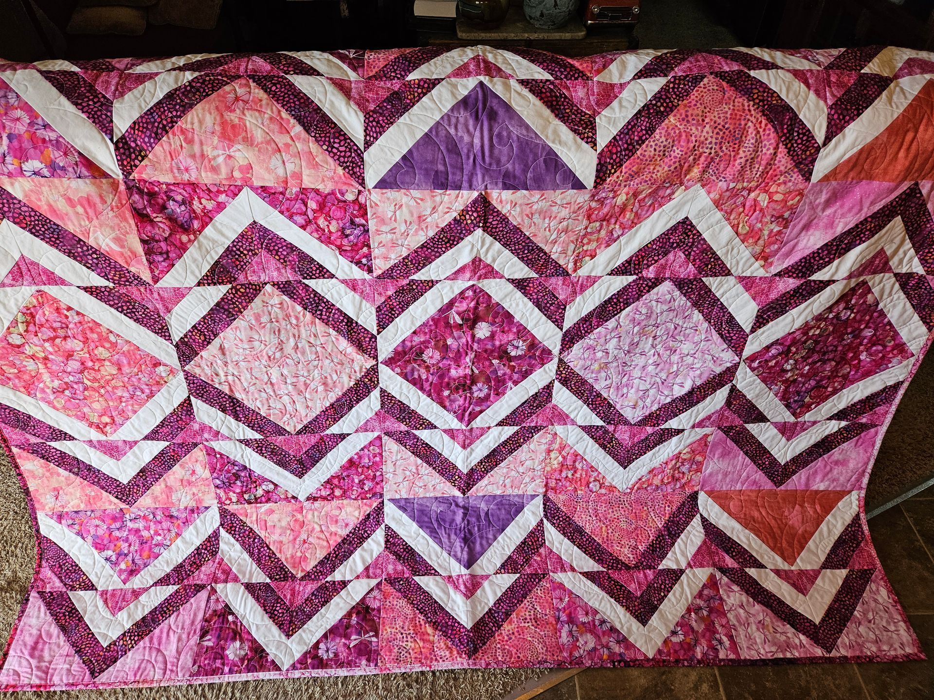 A pink and purple quilt is sitting on a tiled floor.