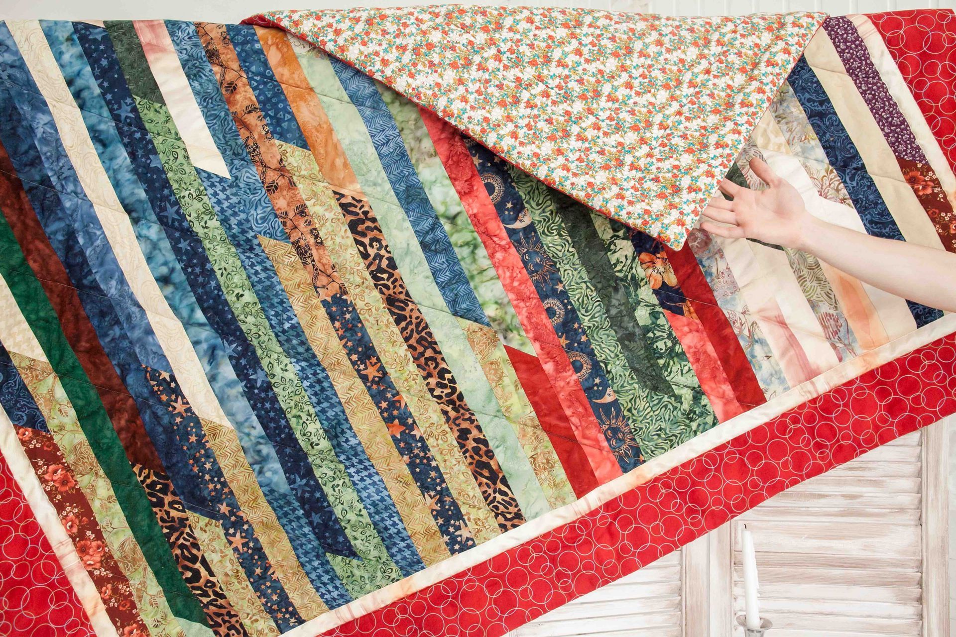 A person is holding a colorful quilt in their hands.