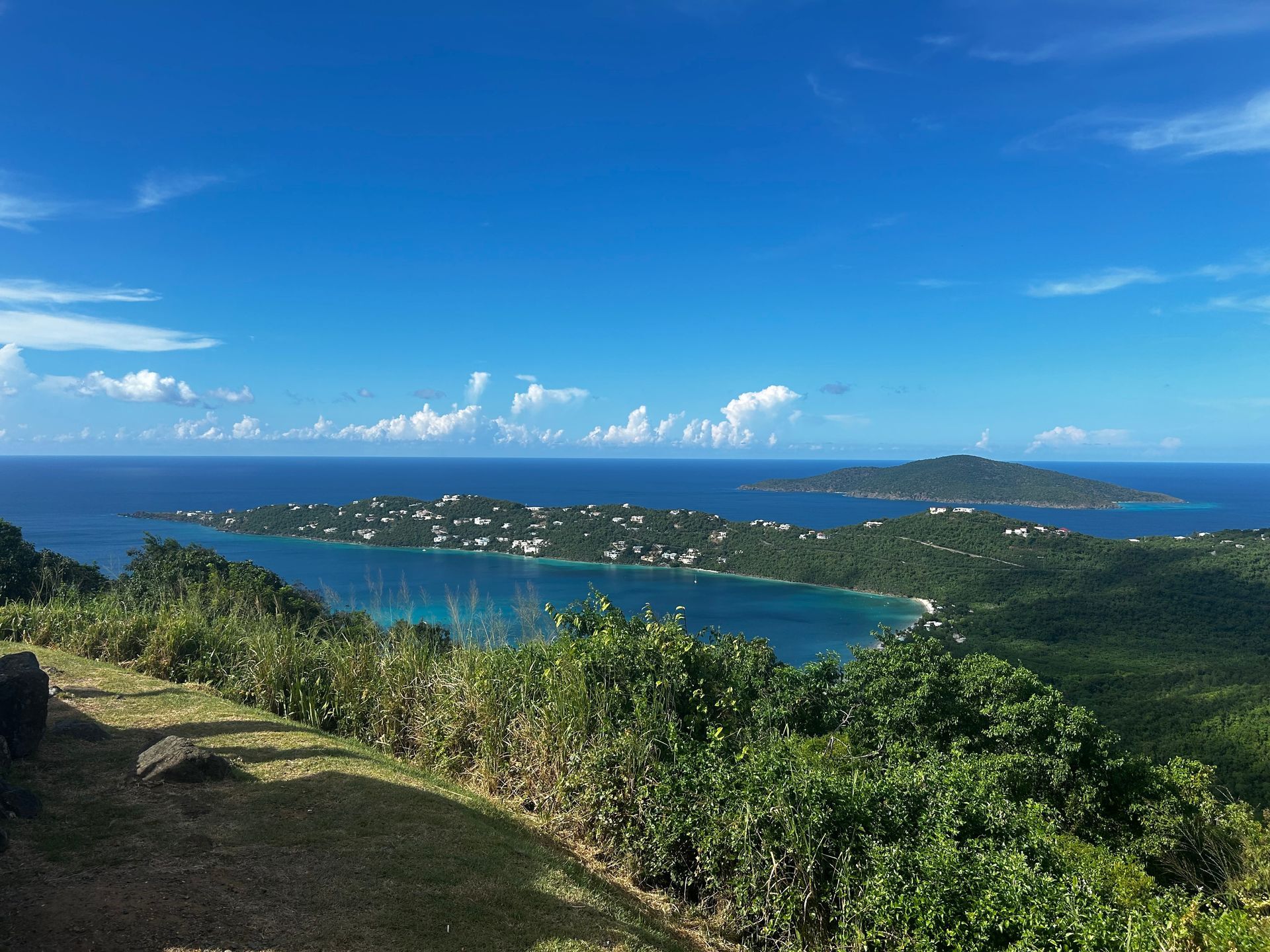 View from hilltop overlooking a bay with turquoise water, islands, and a clear blue sky.