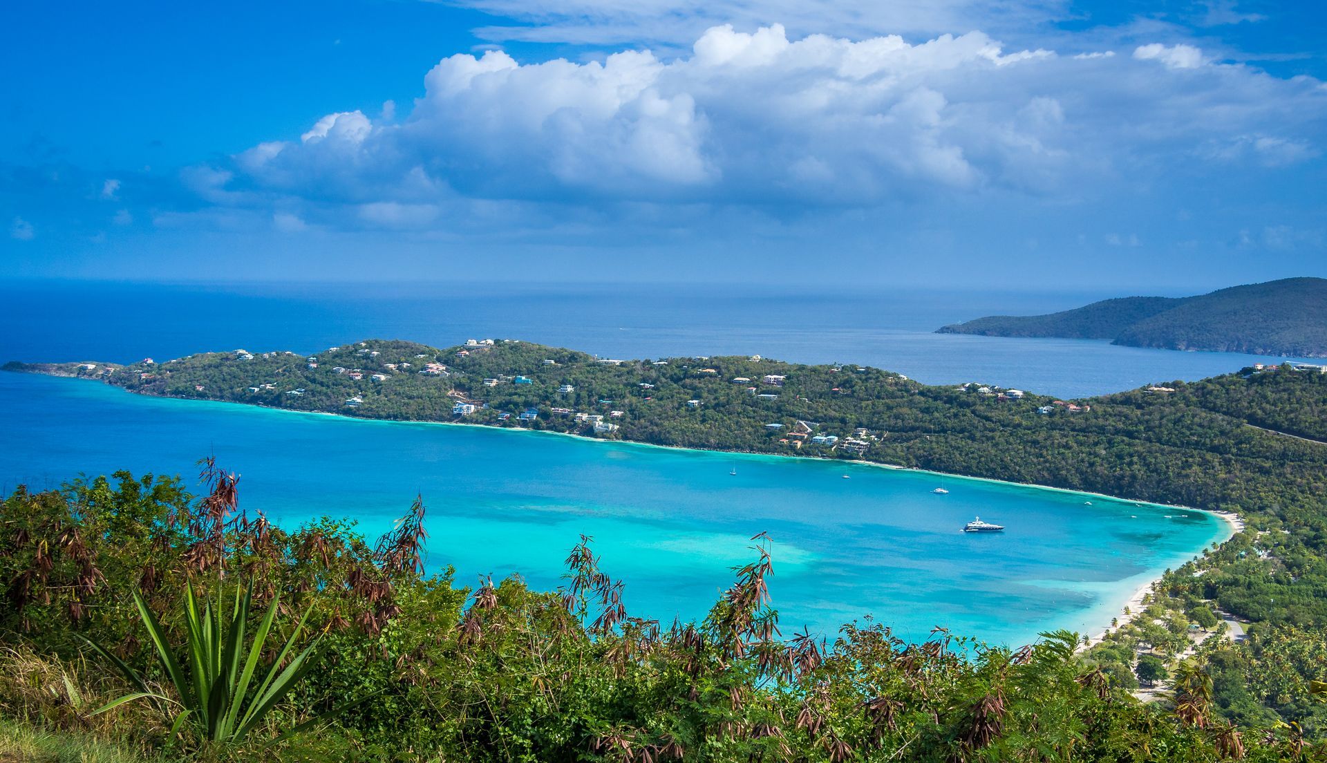 Overlooking a turquoise bay, lush green island with white sand beaches, clear blue sky.