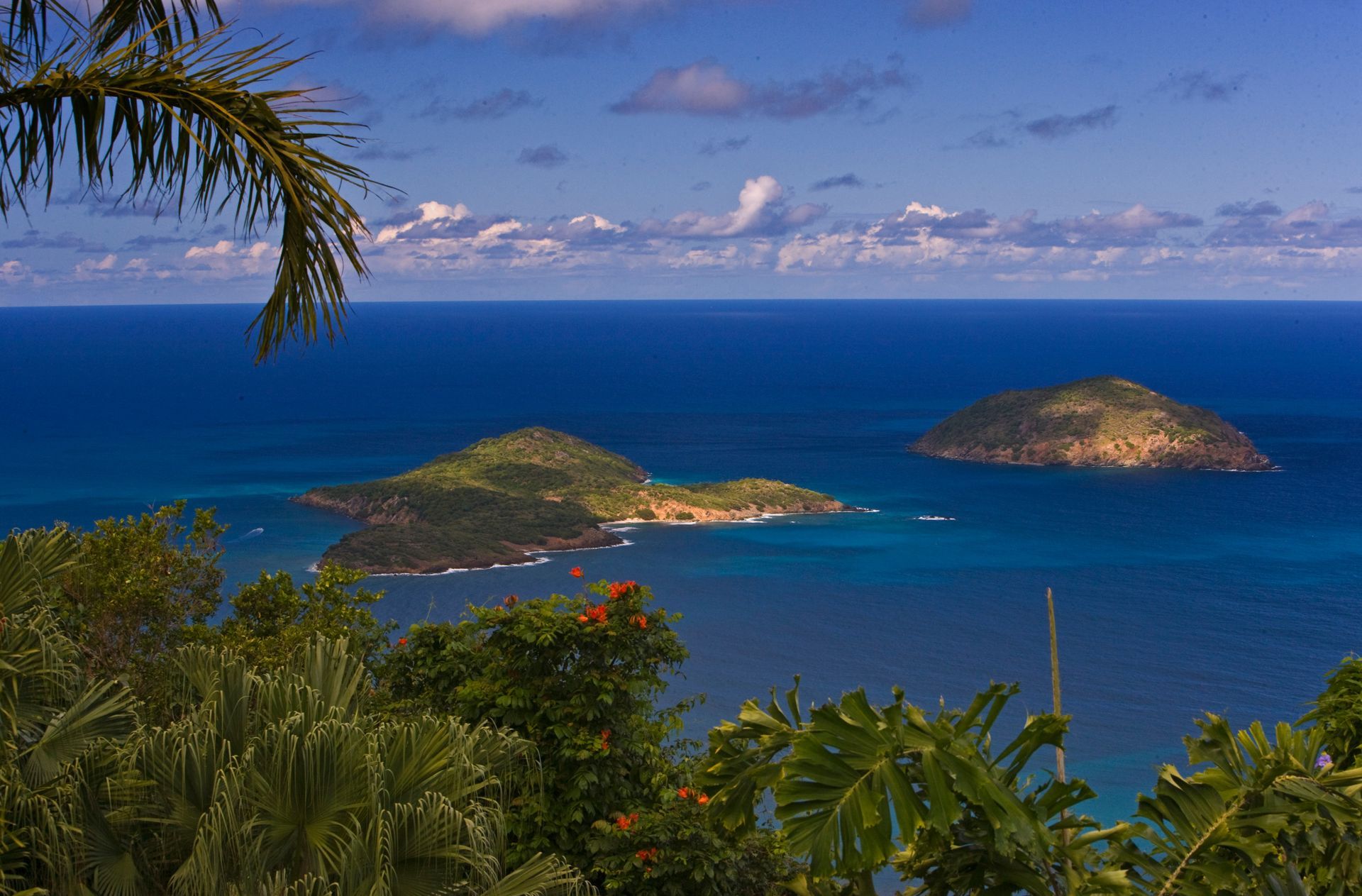 Tropical island view with three green, hilly islands in blue ocean under a blue sky.