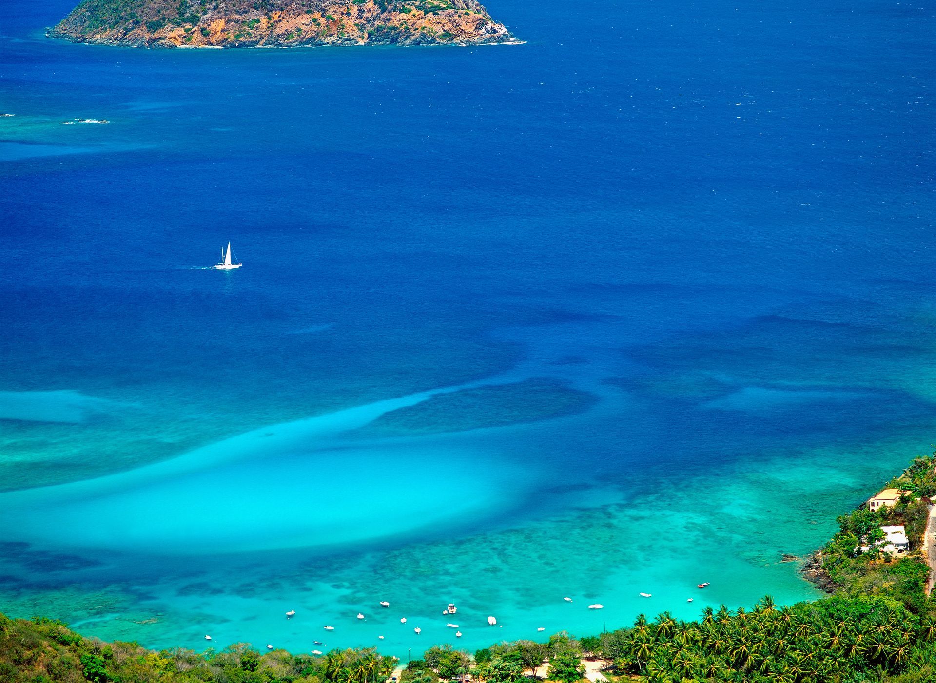 Bright blue ocean view with a sailboat, shallow turquoise water, and an island in the distance.