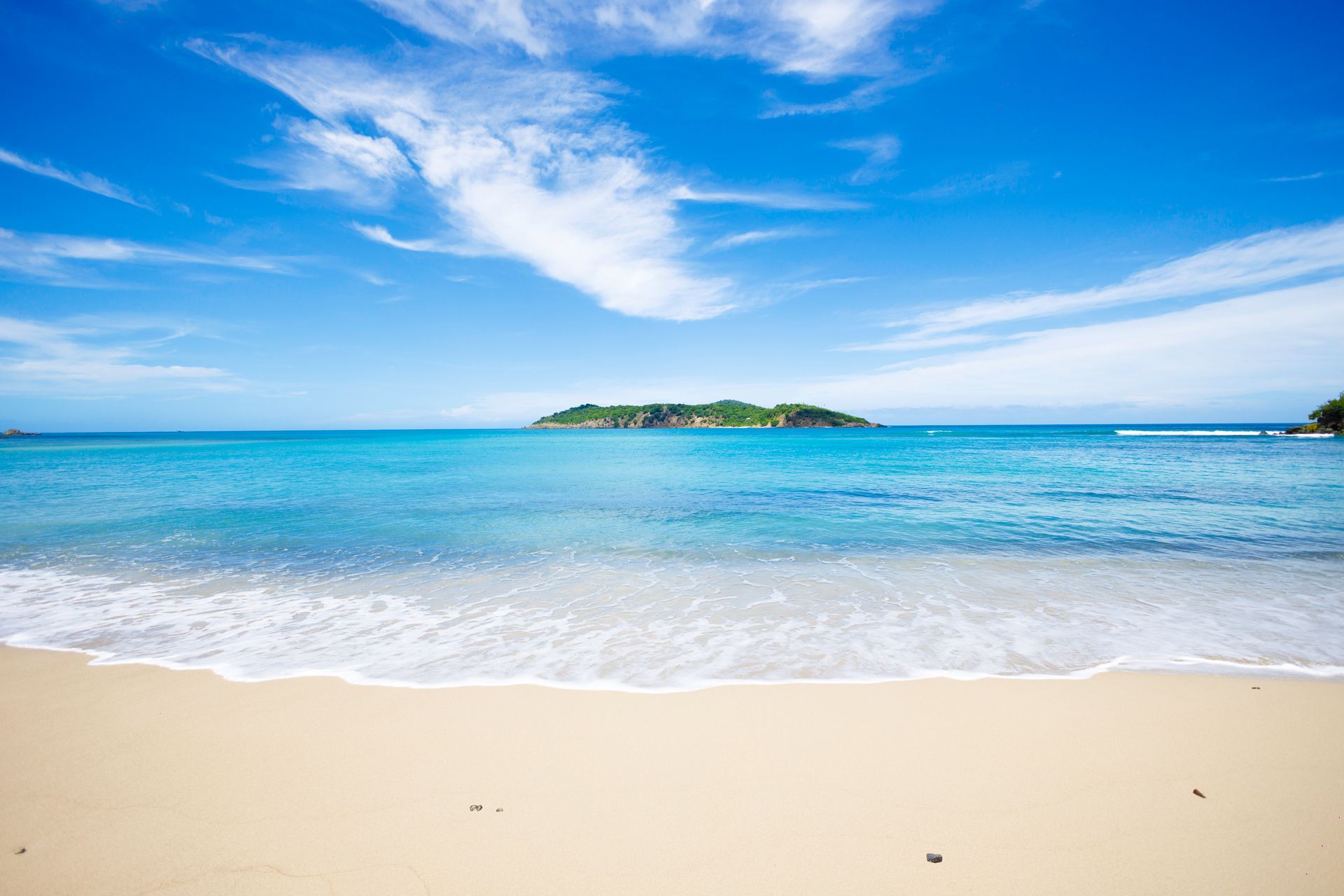 Sandy beach with turquoise water, blue sky, and a small island in the distance.
