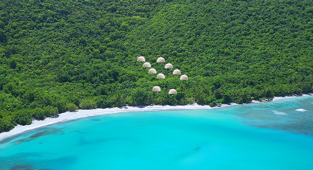 Aerial view of turquoise water meeting a lush green island with several huts.