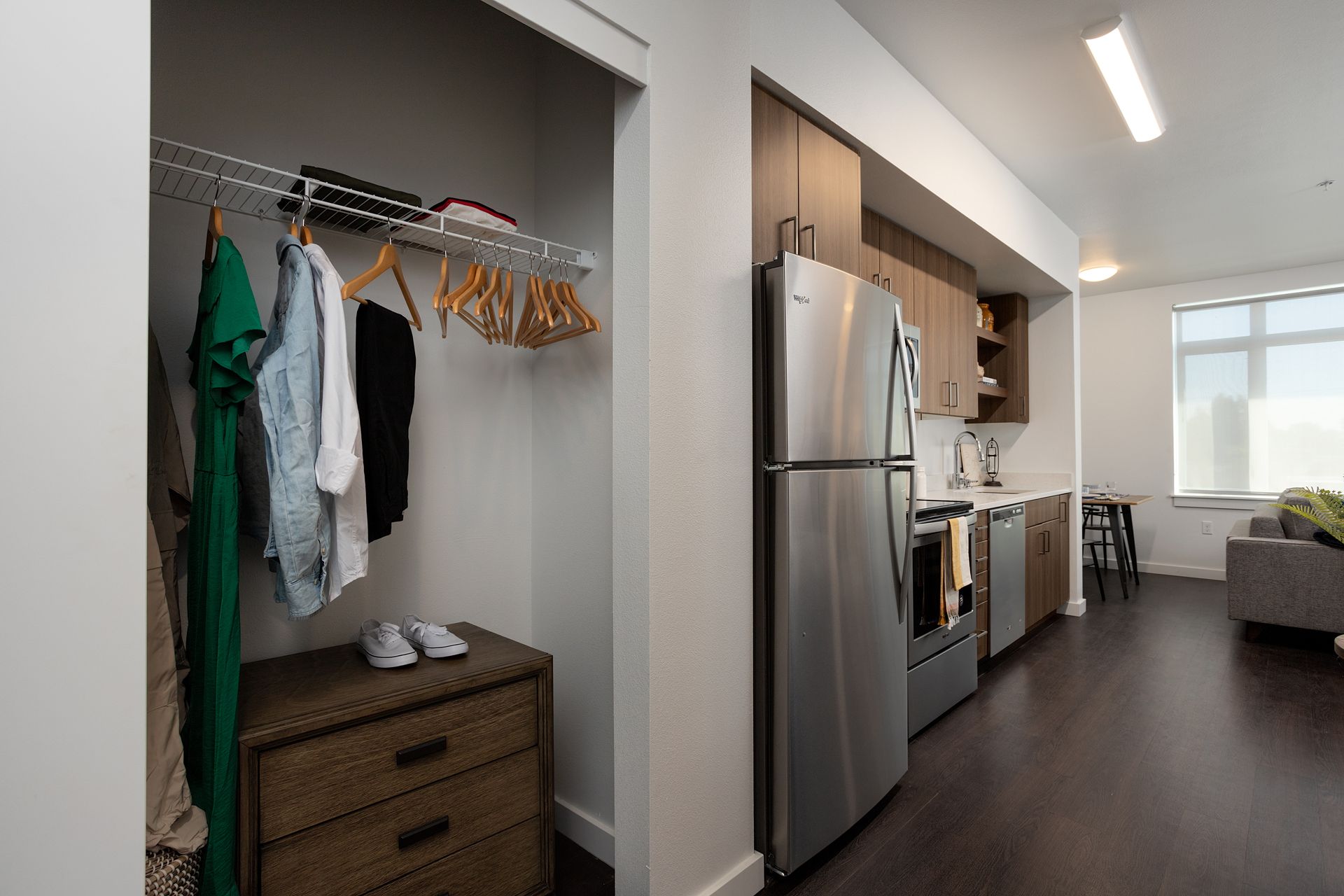 A closet with clothes hanging on it next to a refrigerator and a dresser.