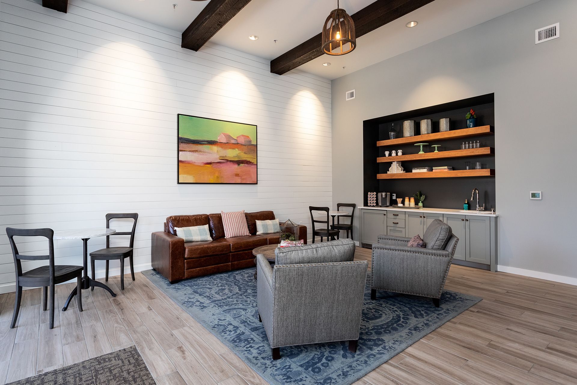 A living room with a couch , chairs , tables and a painting on the wall.
