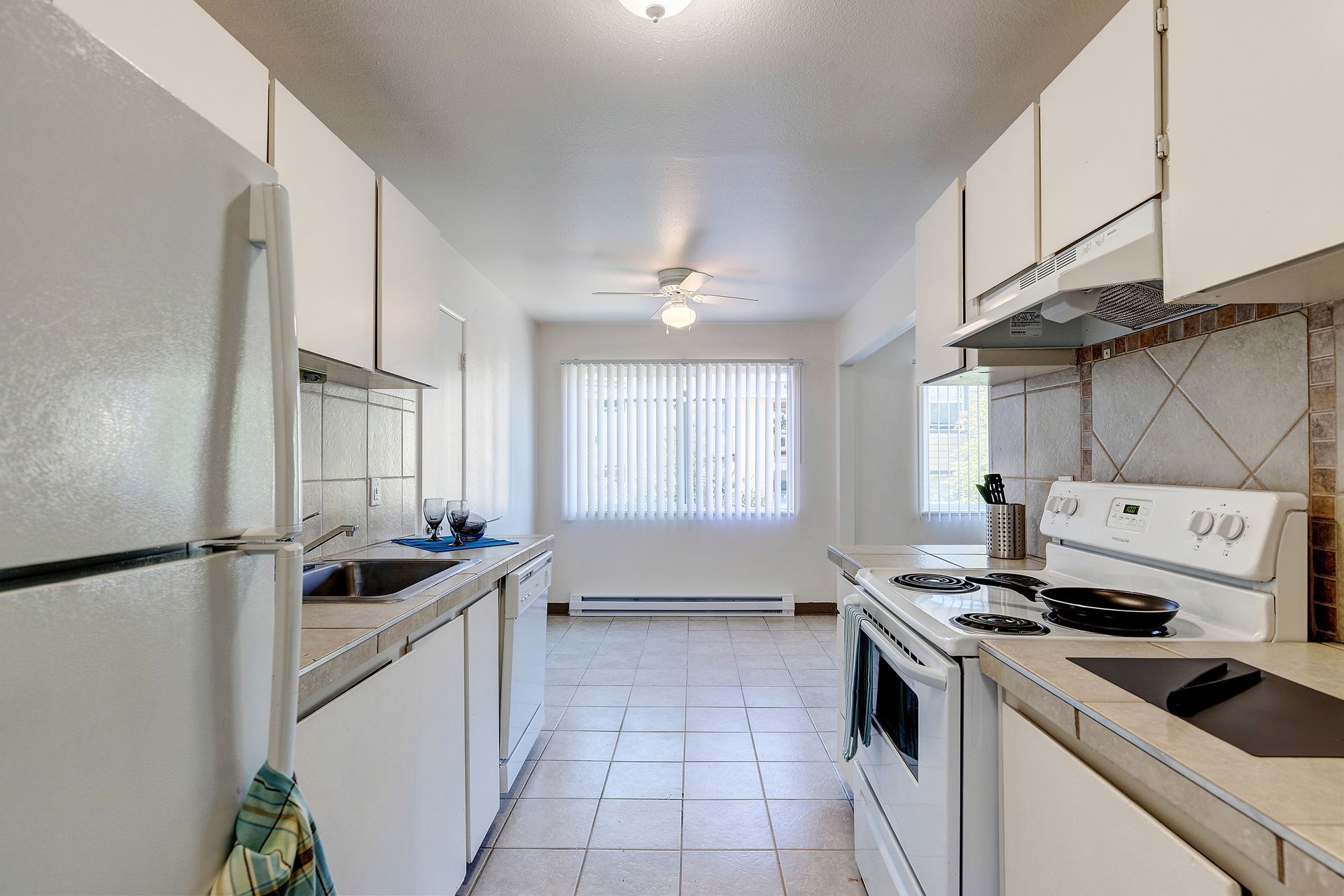 A kitchen with white cabinets , a stove , a refrigerator and a window.
