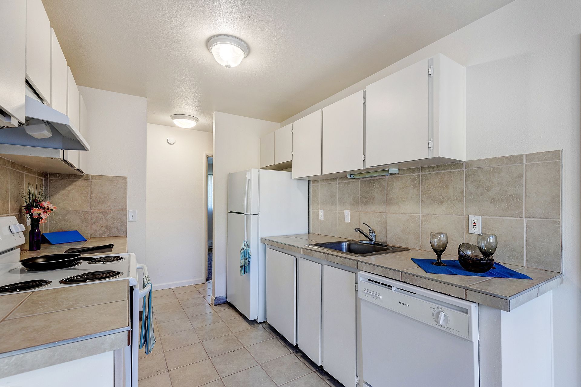 A kitchen with white cabinets , a stove , a refrigerator , and a dishwasher.