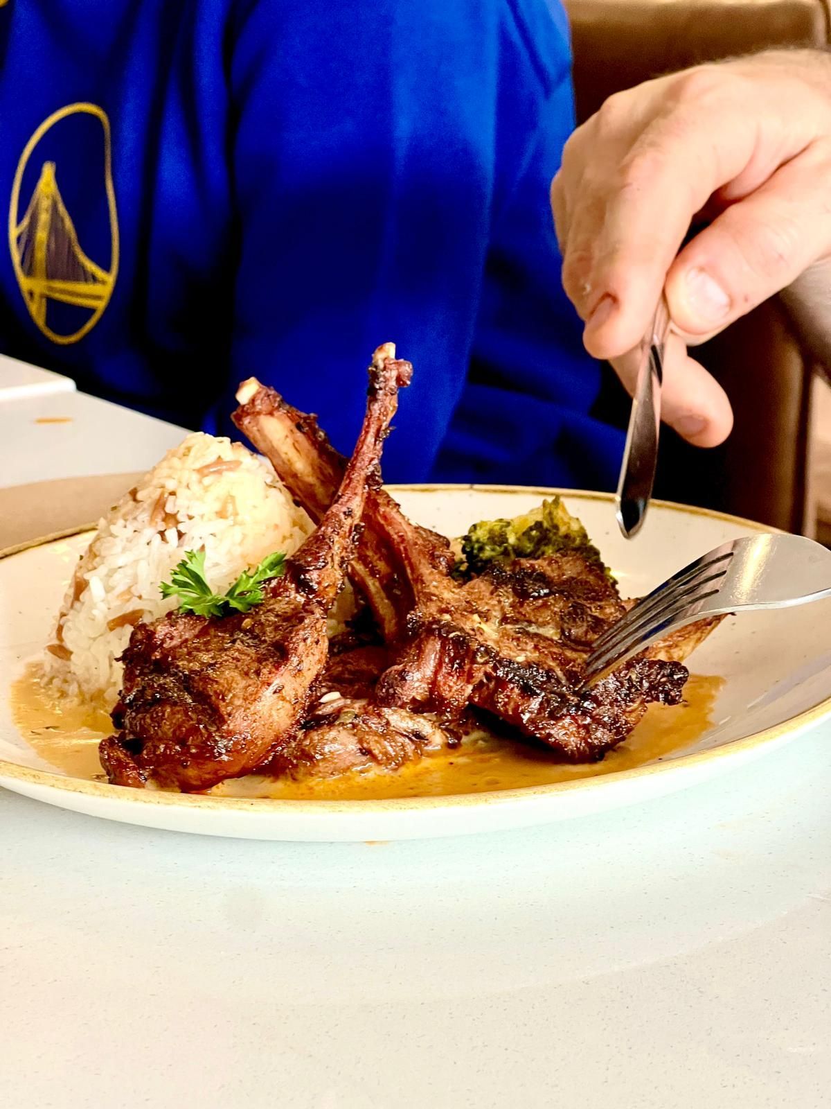 Lamb chops with rice on a plate; a person cuts into the meat with a fork and knife.