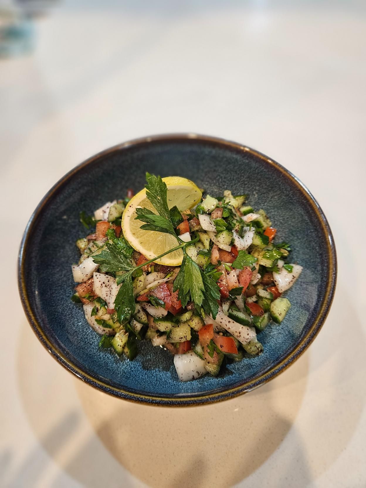 A Bowl of Salad with Tomatoes , Cucumbers , and Parsley on A Table  — Turquoise Turkish Restaurant in Queanbeyan, NSW